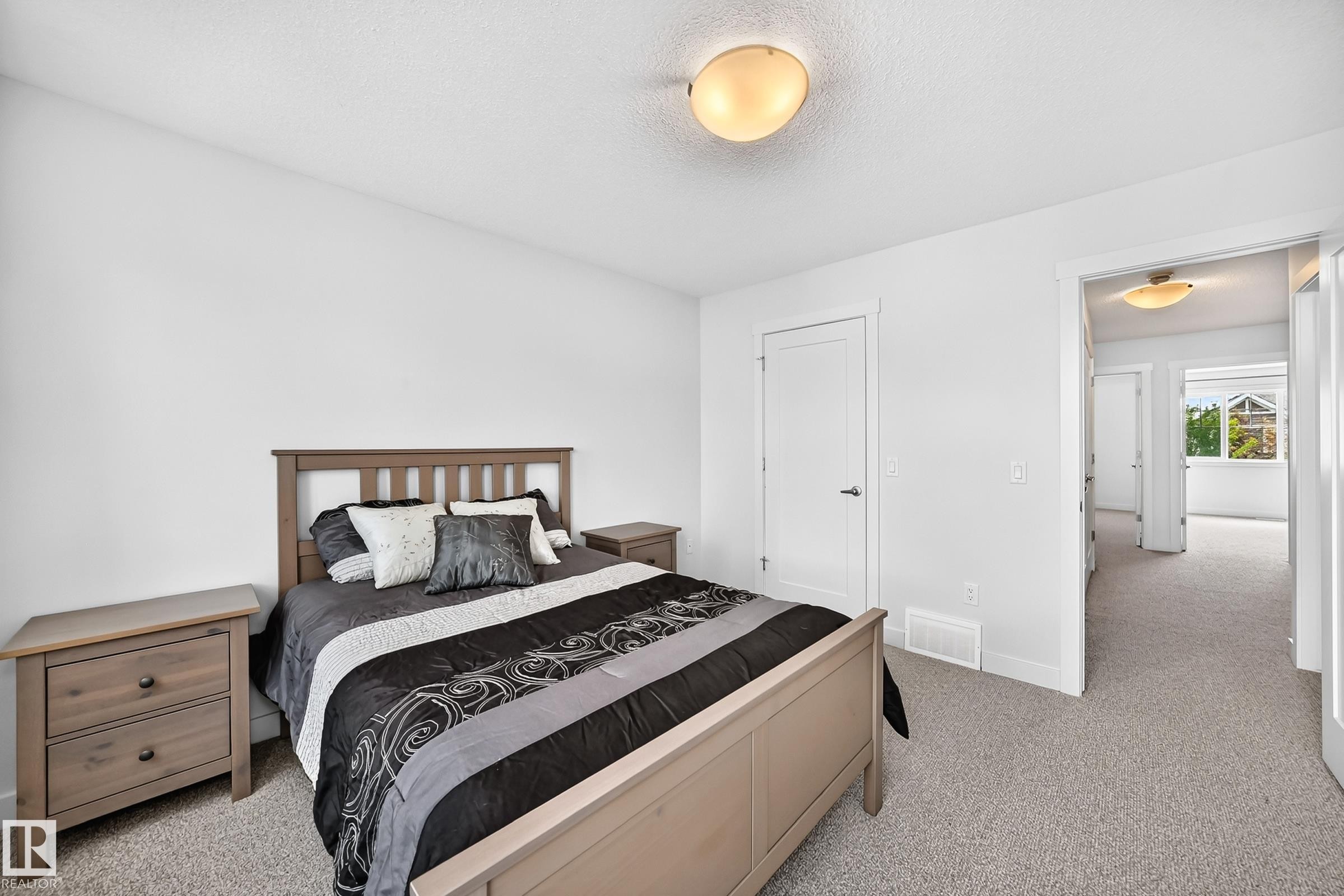 Light-filled bedroom featuring plush carpet flooring, a flush-mount ceiling light fixture, and a white interior door with dark hardware - 2433 Glenridding Boulevard, Edmonton, AB