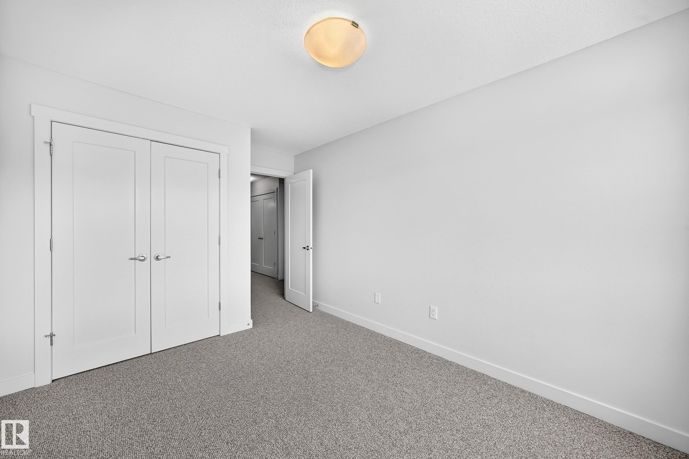Neutral-toned room featuring a light gray textured carpet, white walls, and a white ceiling with a flush-mount light fixture - 2433 Glenridding Boulevard, Edmonton, AB
