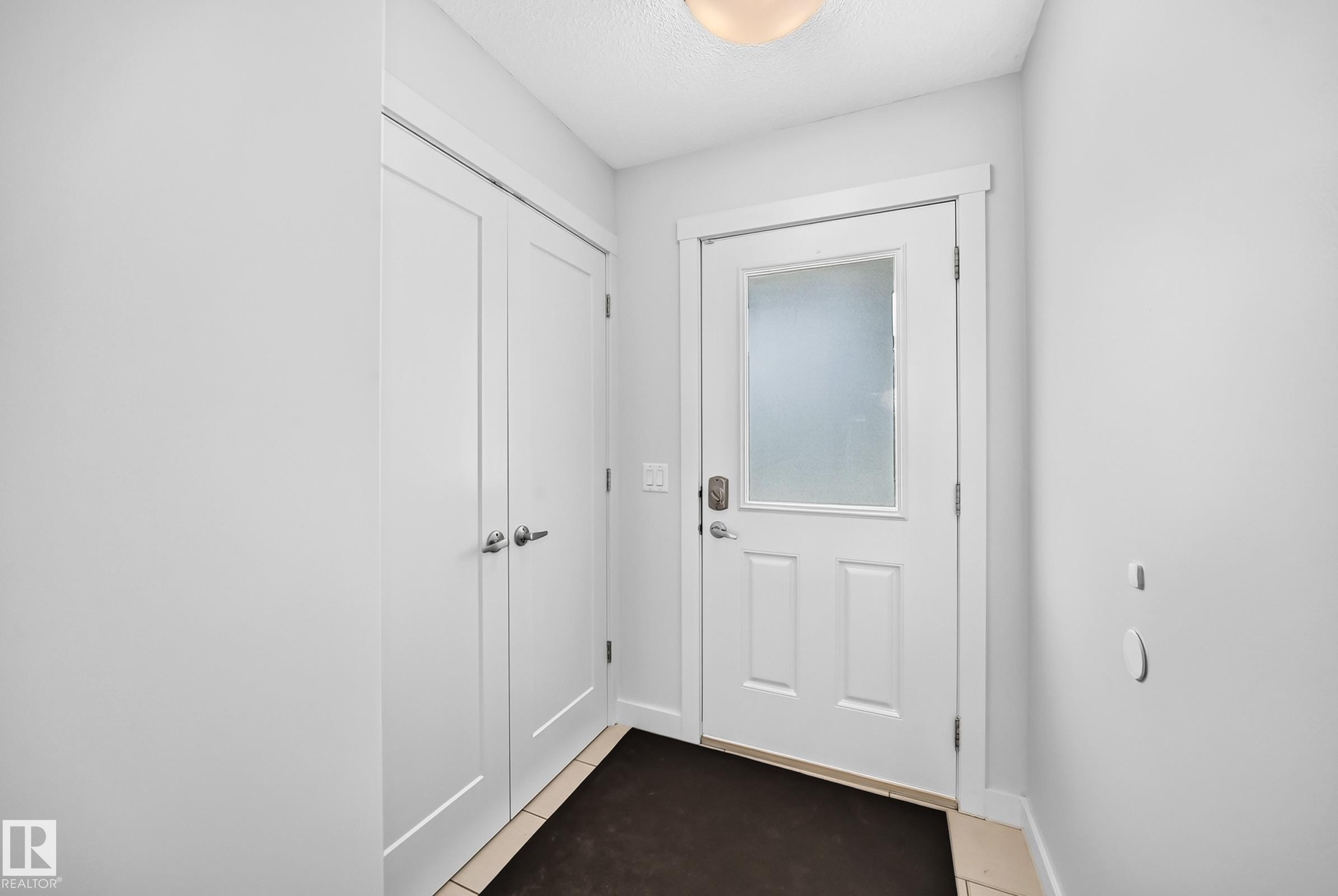 Entryway featuring a white paneled door with frosted glass insert, contrasting dark floor mat, and adjacent double-door closet with satin nickel hardware - 2433 Glenridding Boulevard, Edmonton, AB