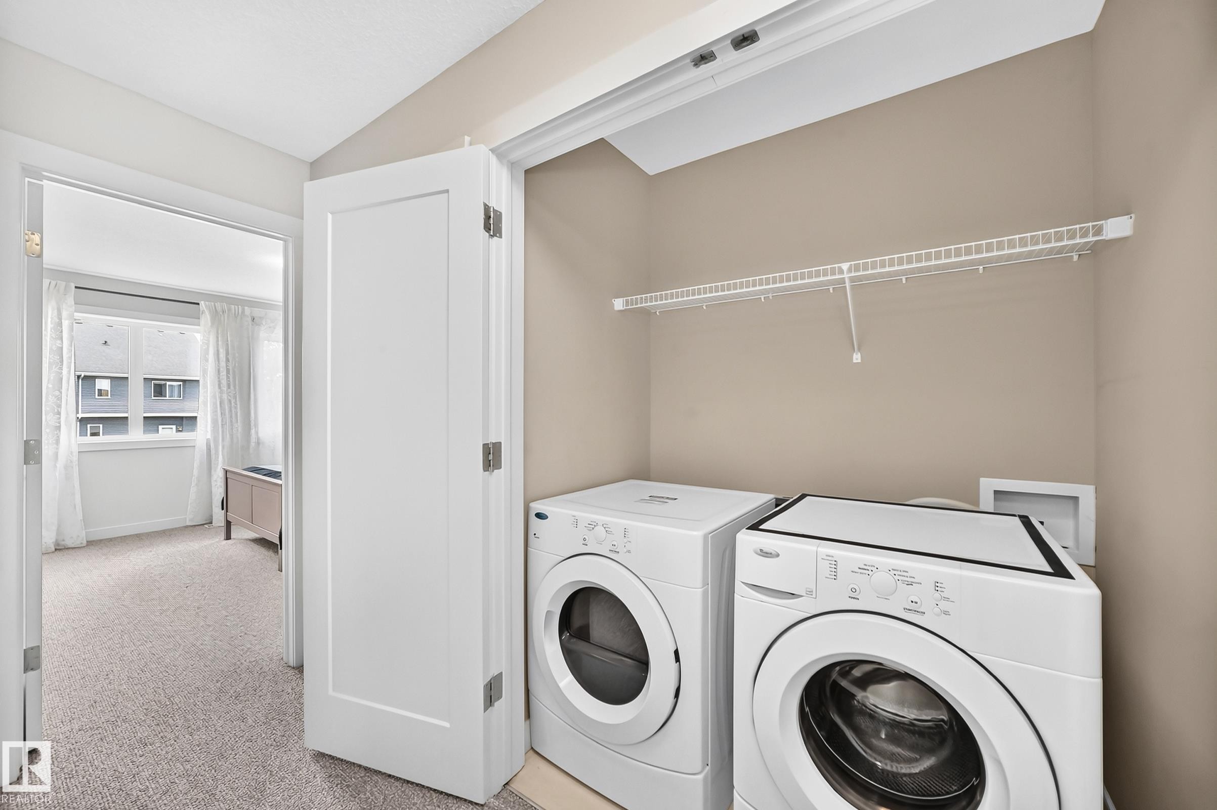 Dedicated laundry area featuring a wire storage shelf, light neutral wall paint, and carpeted flooring - 2433 Glenridding Boulevard, Edmonton, AB