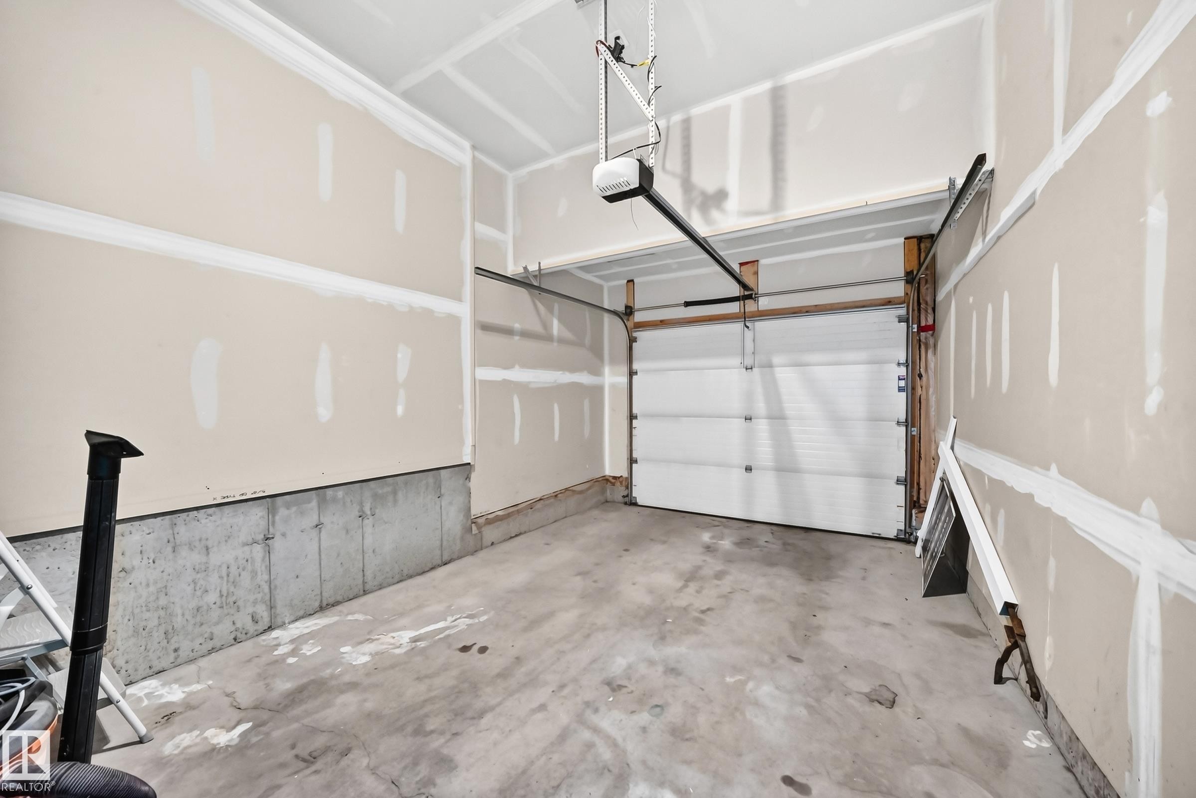 Garage space featuring a concrete floor, an automatic garage door opener, and unfinished drywall walls with a concrete foundation - 2433 Glenridding Boulevard, Edmonton, AB