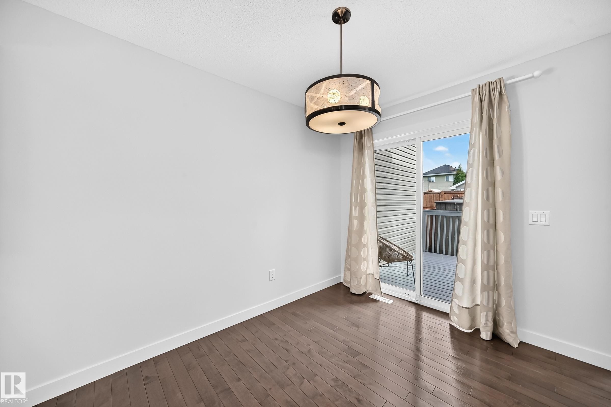 Bright room featuring wood-finish flooring, a contemporary drum pendant light, and a sliding glass door providing access to an outdoor deck - 2433 Glenridding Boulevard, Edmonton, AB