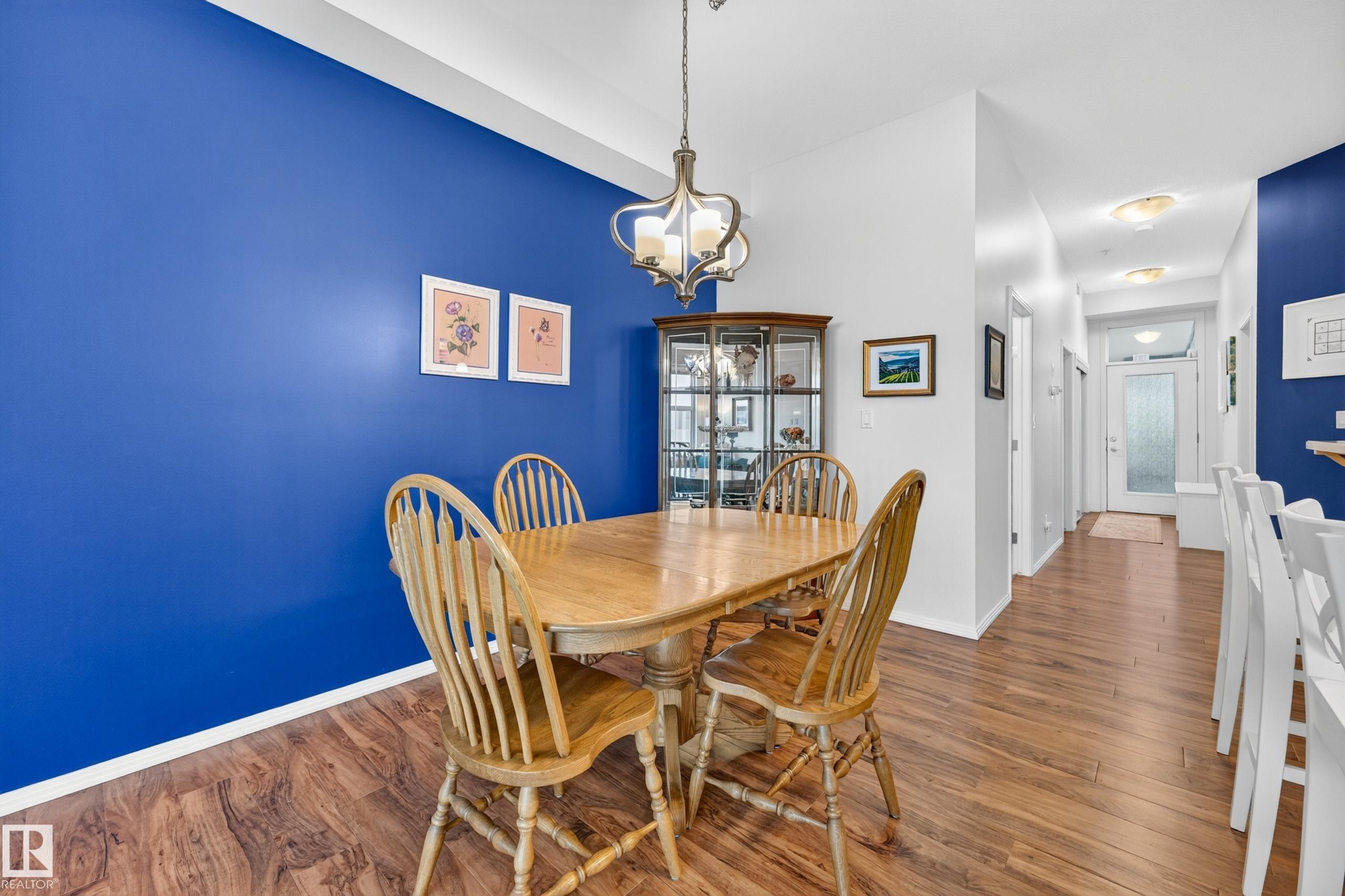 Dining area featuring a prominent blue accent wall, wood-finish flooring, and a decorative ceiling light fixture - #410 10531 117 St Nw, Edmonton, AB