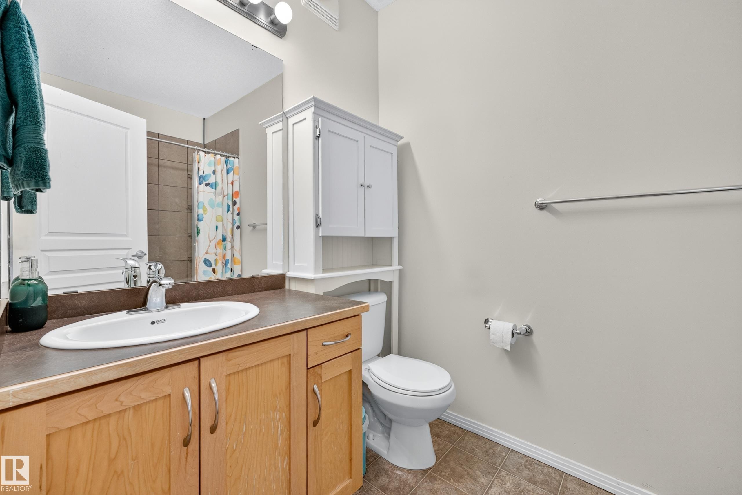 Bathroom featuring a light-toned wood-finish vanity with an integrated sink and dark countertop, complemented by a large wall mirror and a three-light fixture - #410 10531 117 St Nw, Edmonton, AB