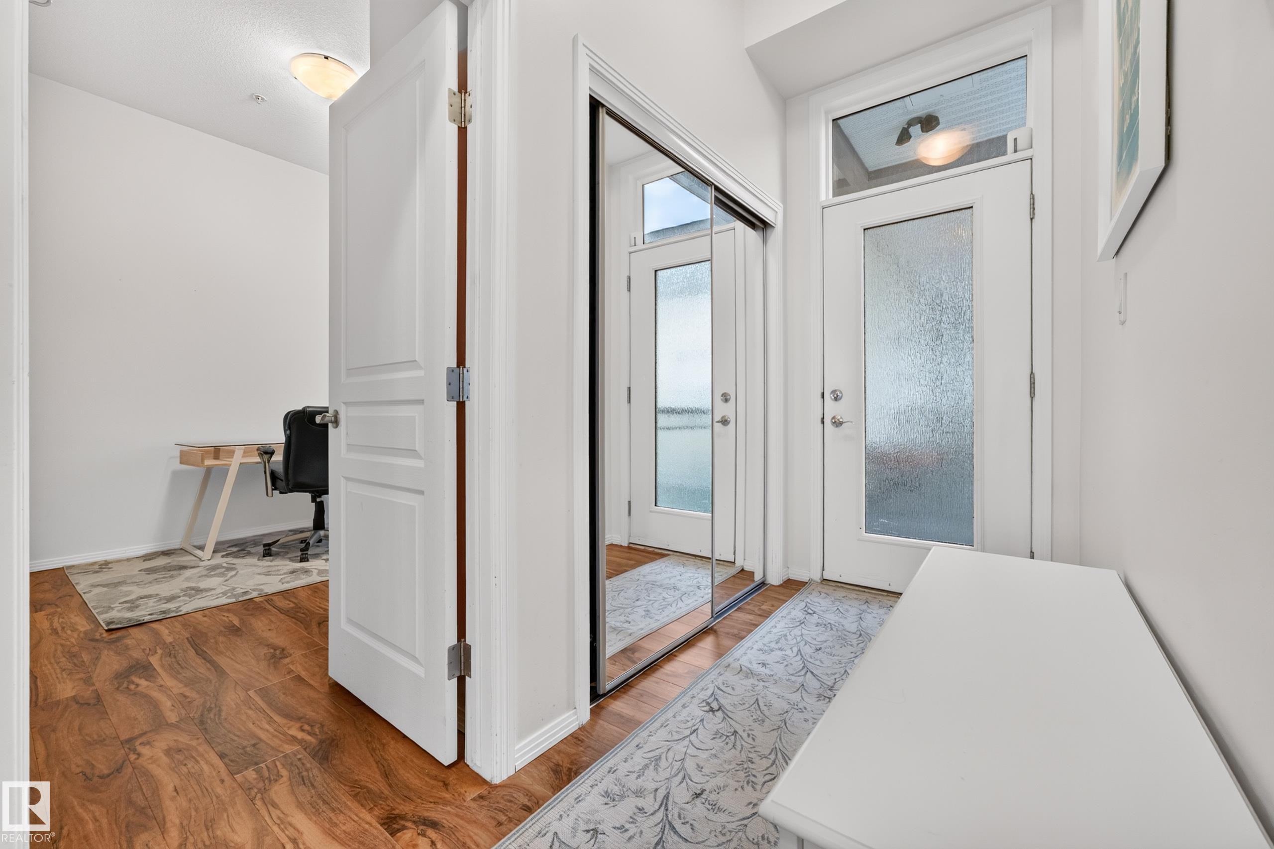 Entryway featuring wood-finish flooring, a full-lite door with frosted glass, and a transom window - #410 10531 117 St Nw, Edmonton, AB