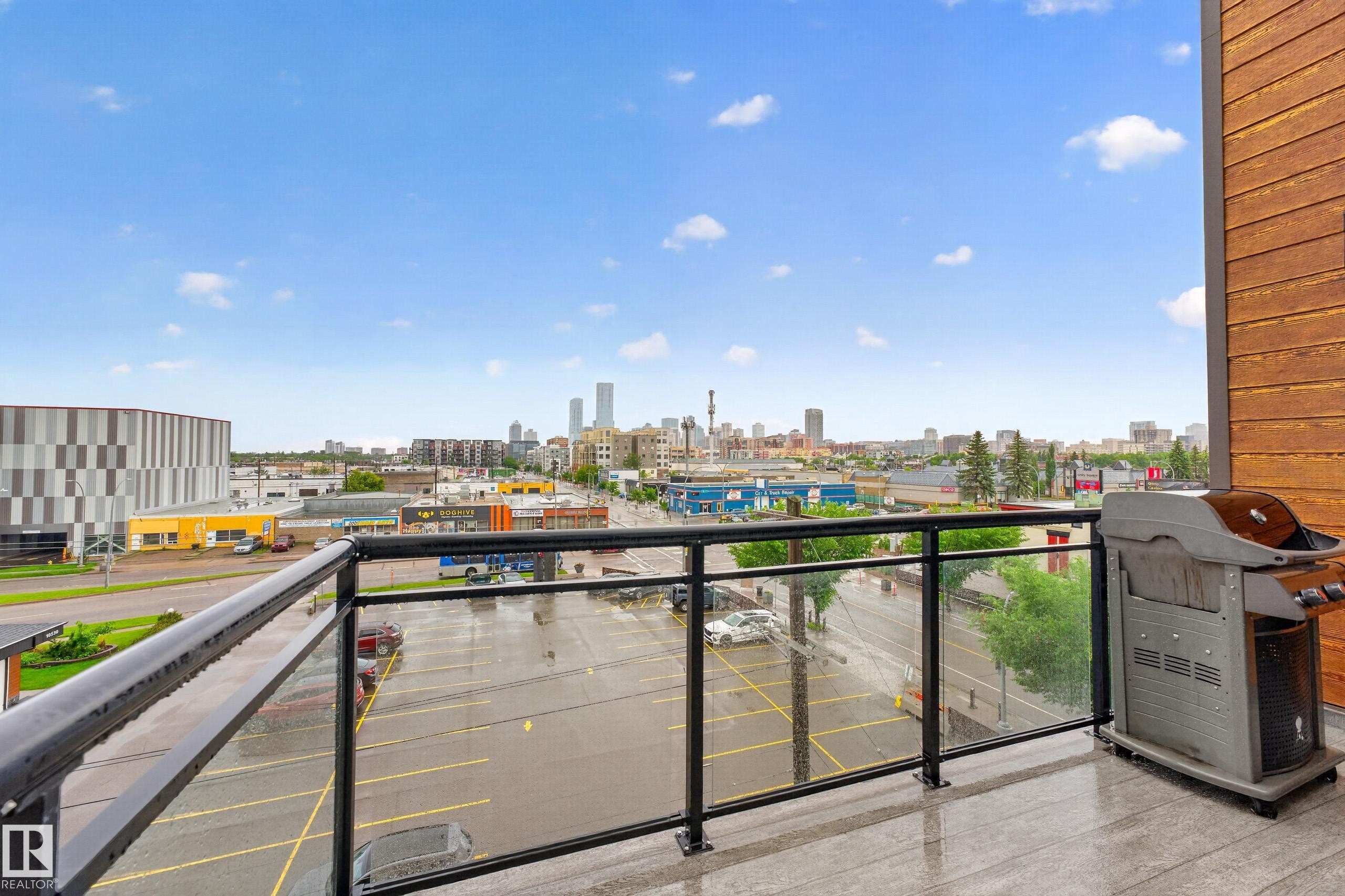 Expansive outdoor balcony featuring a glass and metal railing, wood-look siding, and a cityscape backdrop - #410 10531 117 St Nw, Edmonton, AB