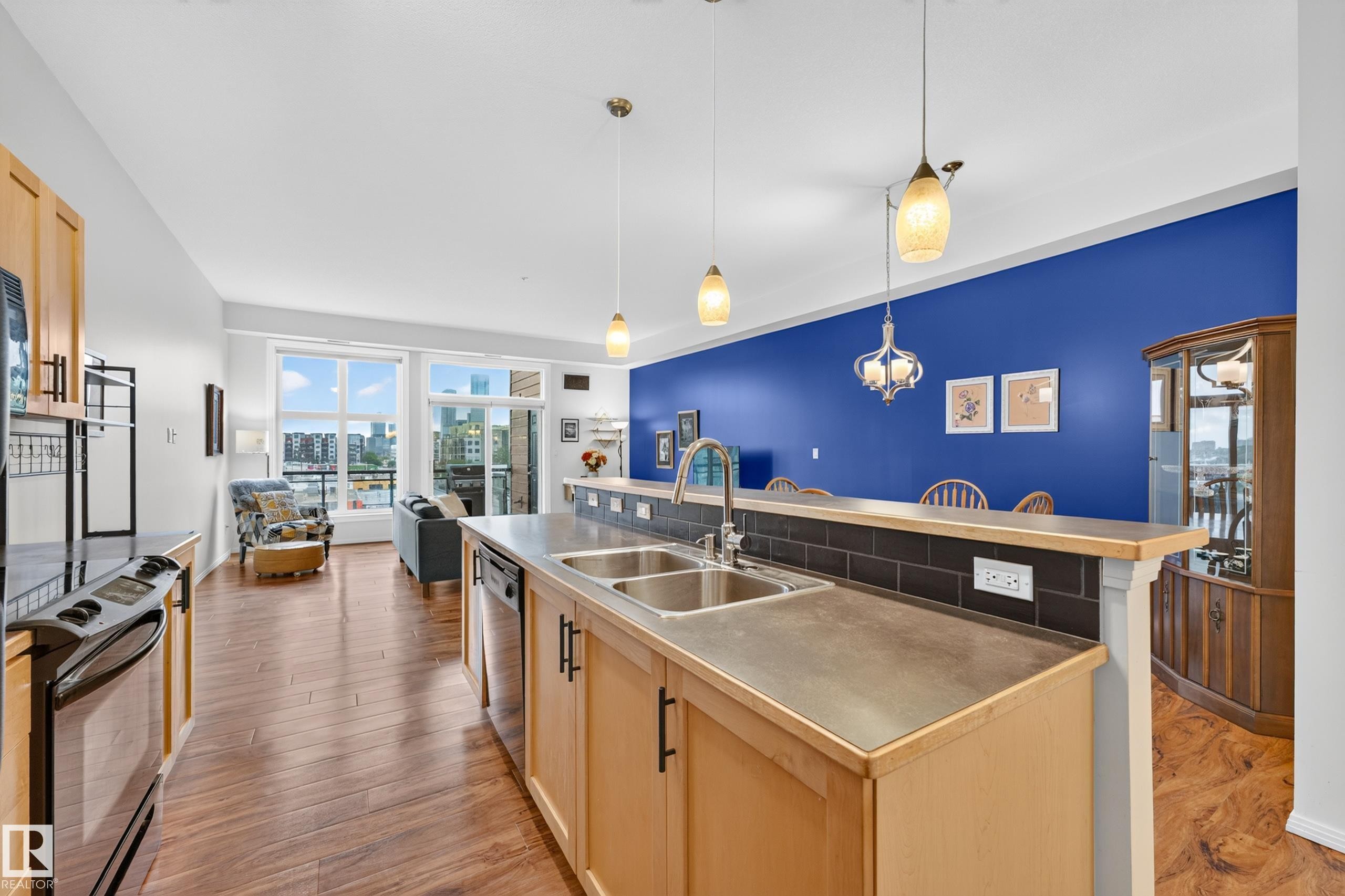 Open-concept living space featuring wood-finish flooring and ample natural light from large windows - #410 10531 117 St Nw, Edmonton, AB