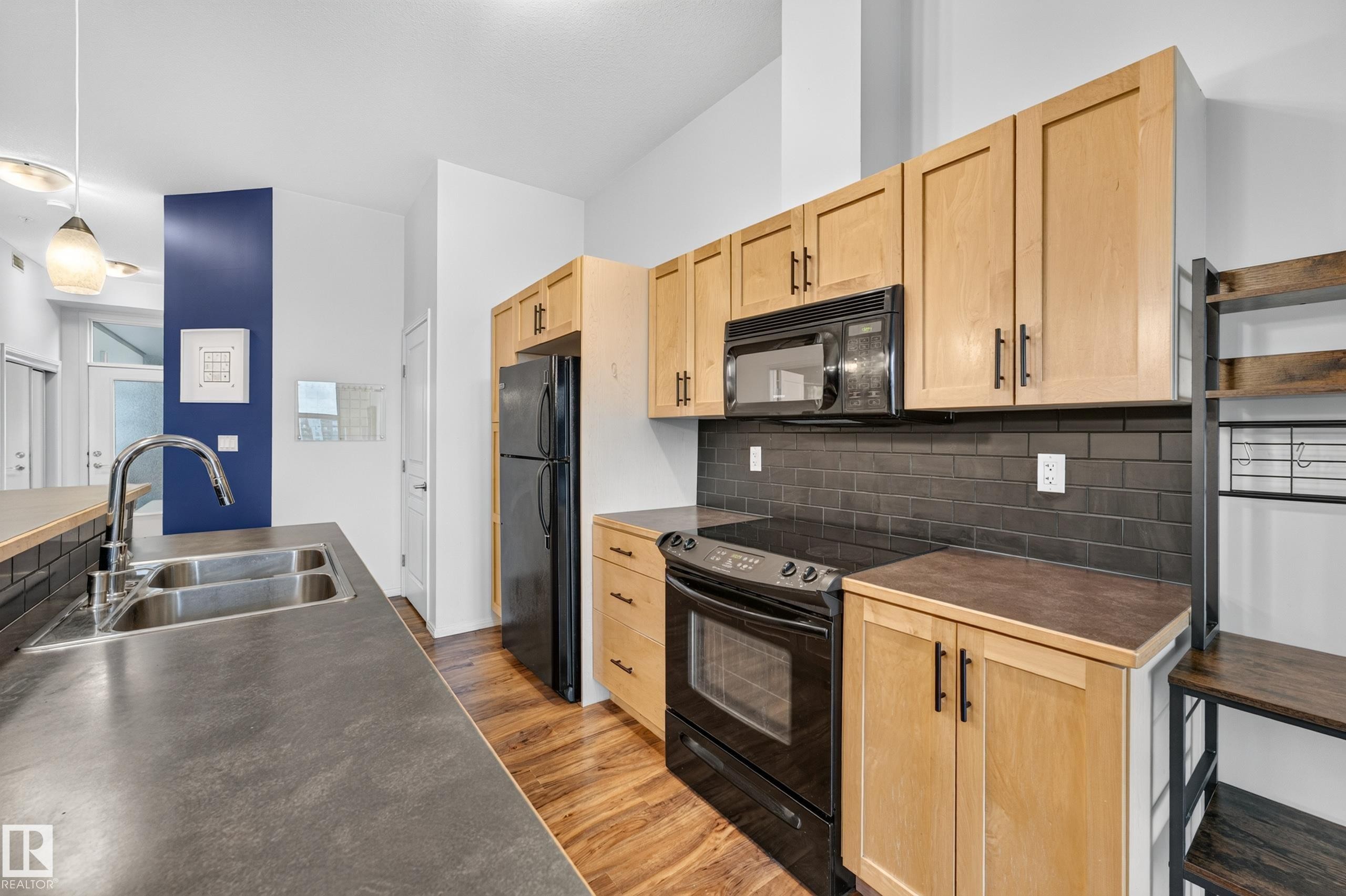 Kitchen featuring wood-finish cabinetry, black subway tile backsplash, black appliances, and a double basin stainless steel sink with a high-arch faucet - #410 10531 117 St Nw, Edmonton, AB