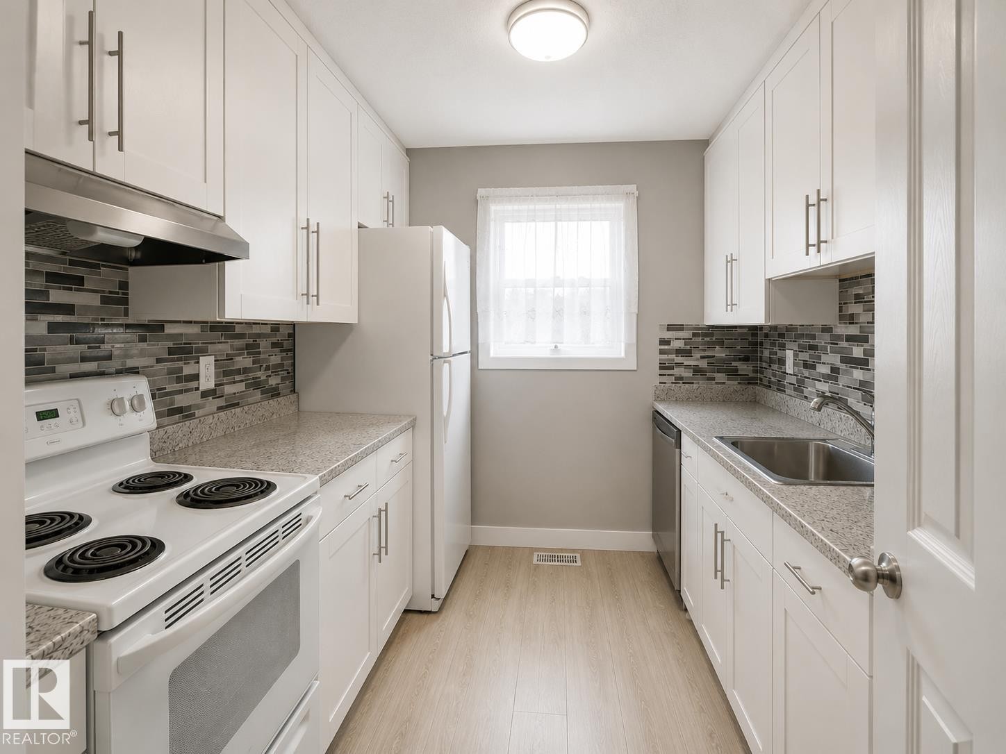 Galley kitchen featuring white cabinetry, light wood-finish flooring, mosaic tile backsplash, and light-toned countertops - 6348 180St, Edmonton, AB