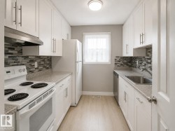 Galley kitchen featuring white cabinetry, light wood-finish flooring, mosaic tile backsplash, and light-toned countertops -