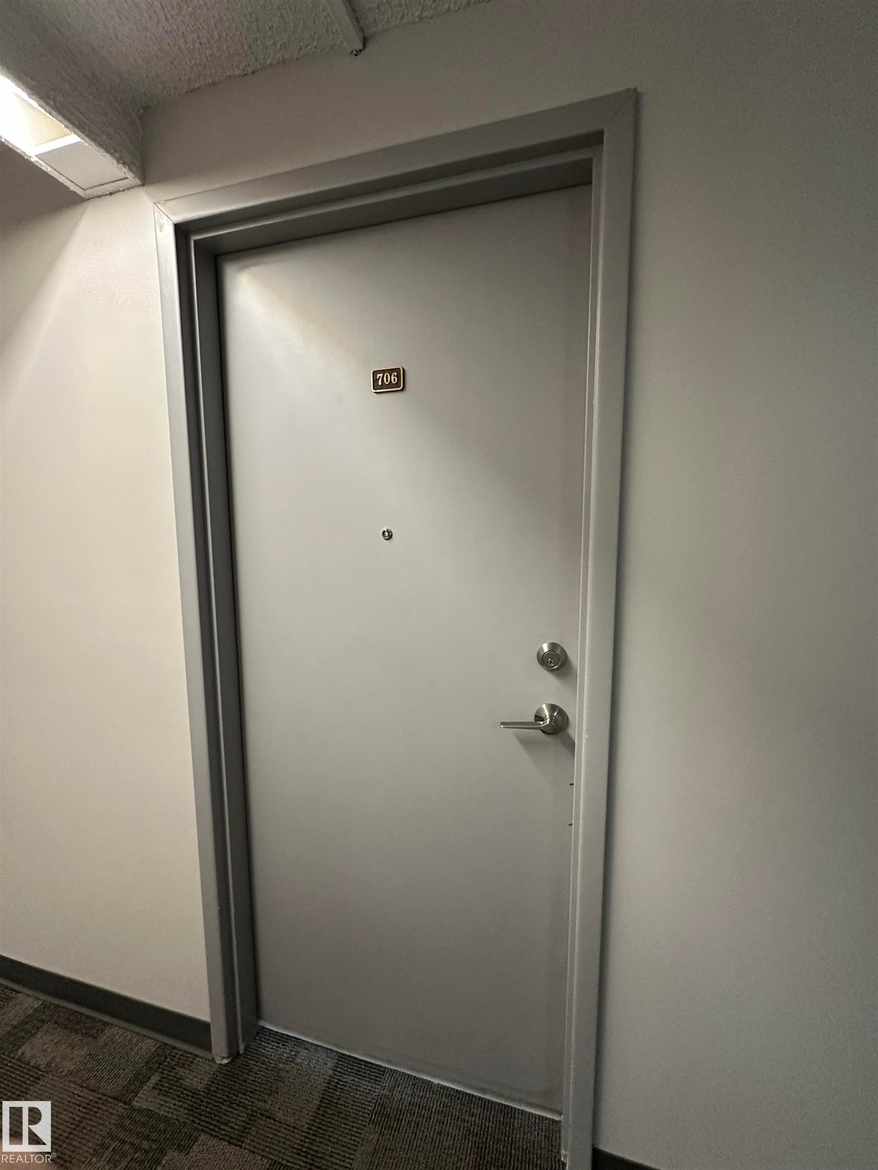 Solid core entry door with matte silver hardware, peephole, and apartment number plate - #706 10145 109 St Nw, Edmonton, AB