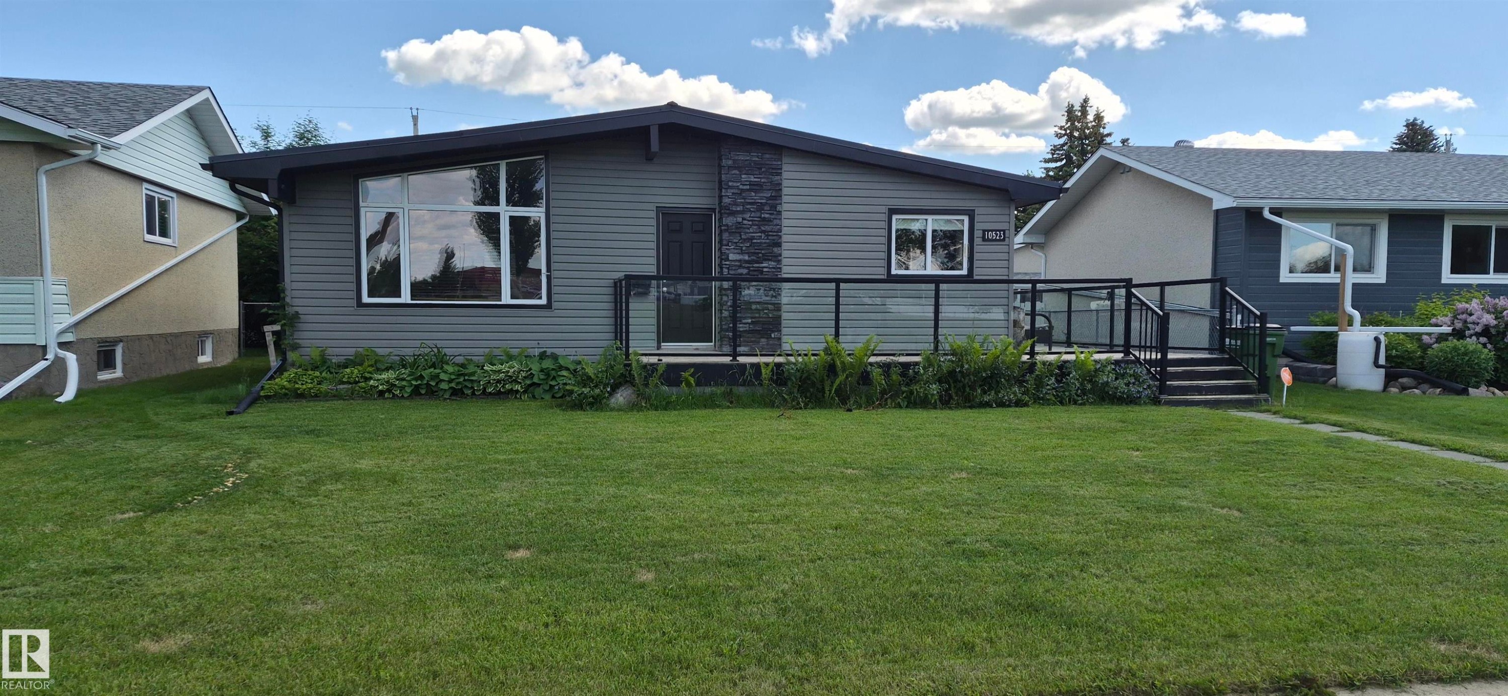 Contemporary-style residence featuring grey horizontal siding and a prominent stone facade accent - 10523 105 Street, Westlock, AB