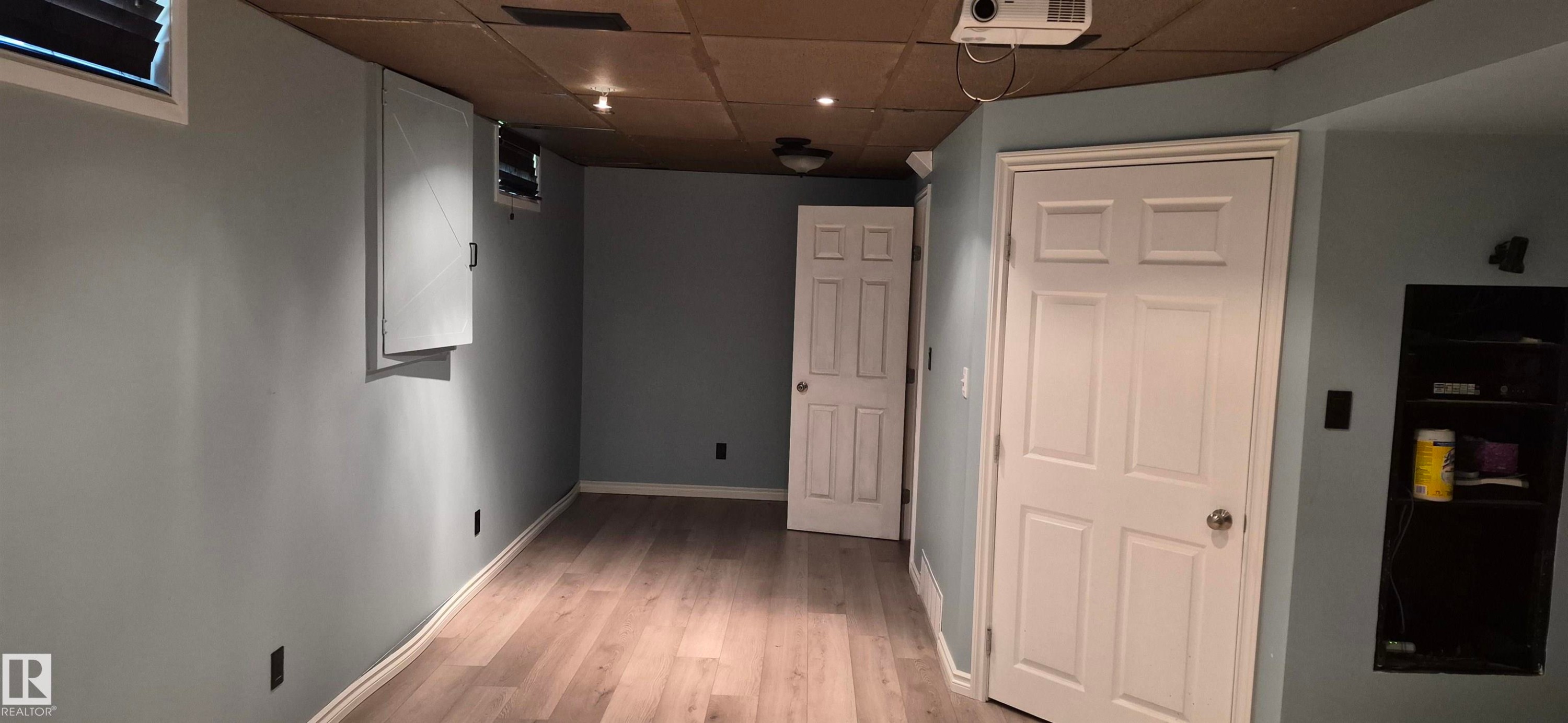 Room featuring wood-finish flooring, light blue walls, and multiple paneled doors - 10523 105 Street, Westlock, AB