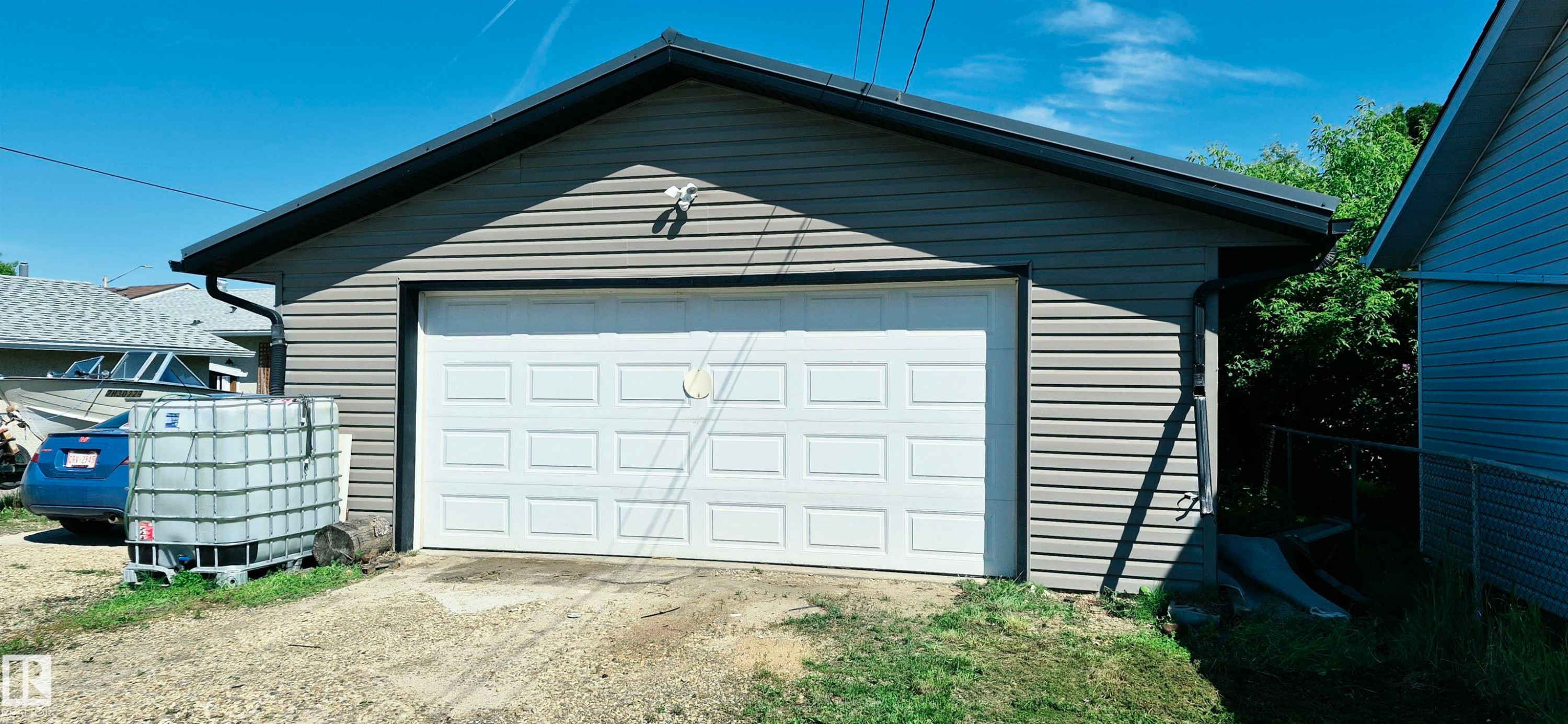 Detached garage featuring horizontal siding, a paneled overhead door, and a dark-toned roofline - 10523 105 Street, Westlock, AB