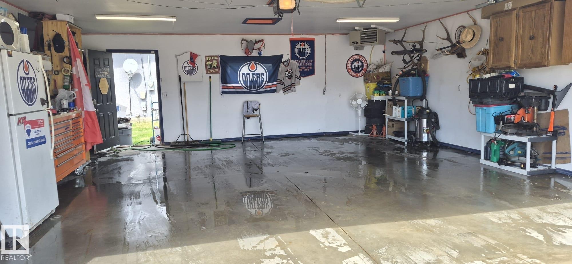 Spacious garage featuring a durable concrete floor, an overhead garage door, built-in wall cabinetry, and a side access door - 10523 105 Street, Westlock, AB