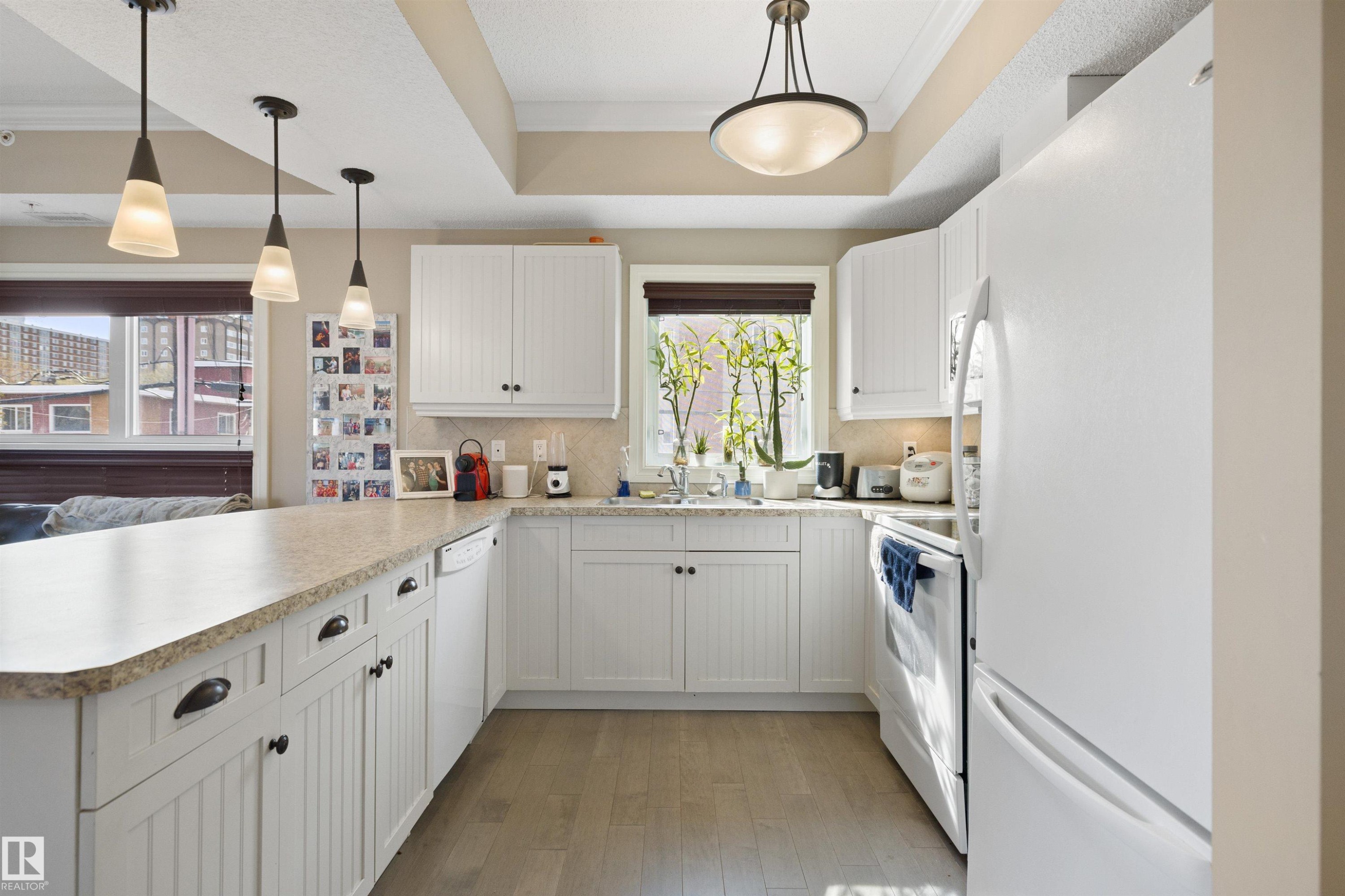 Bright kitchen featuring white cabinetry, light wood-finish flooring, a patterned countertop, and built-in appliances including a refrigerator, oven, and dishwasher - #206 10232 115 St Nw, Edmonton, AB