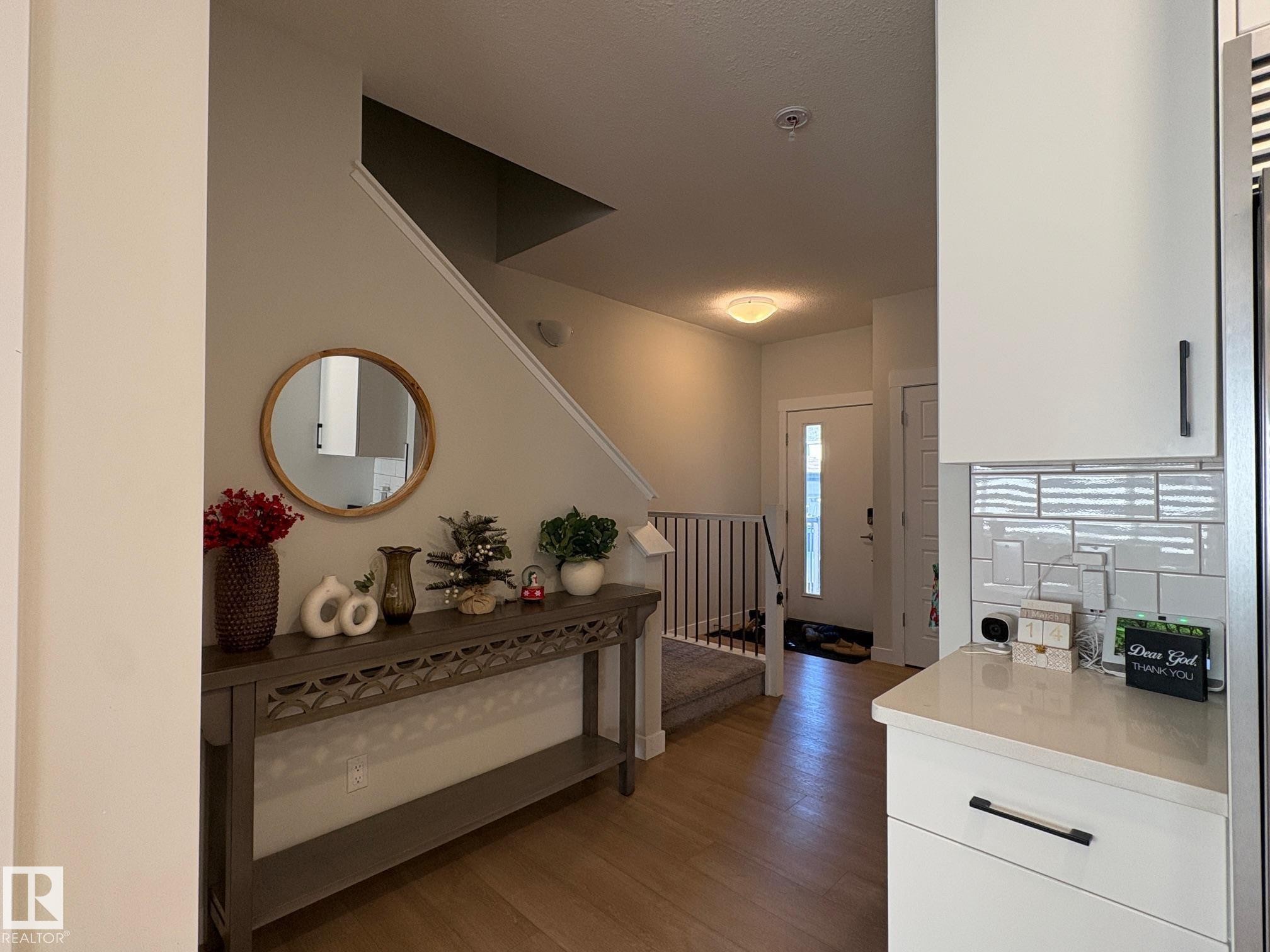 Entryway featuring wood-finish flooring, a white front door with vertical paneled glass, and a staircase with metal balusters - 9952 227 Street, Edmonton, AB