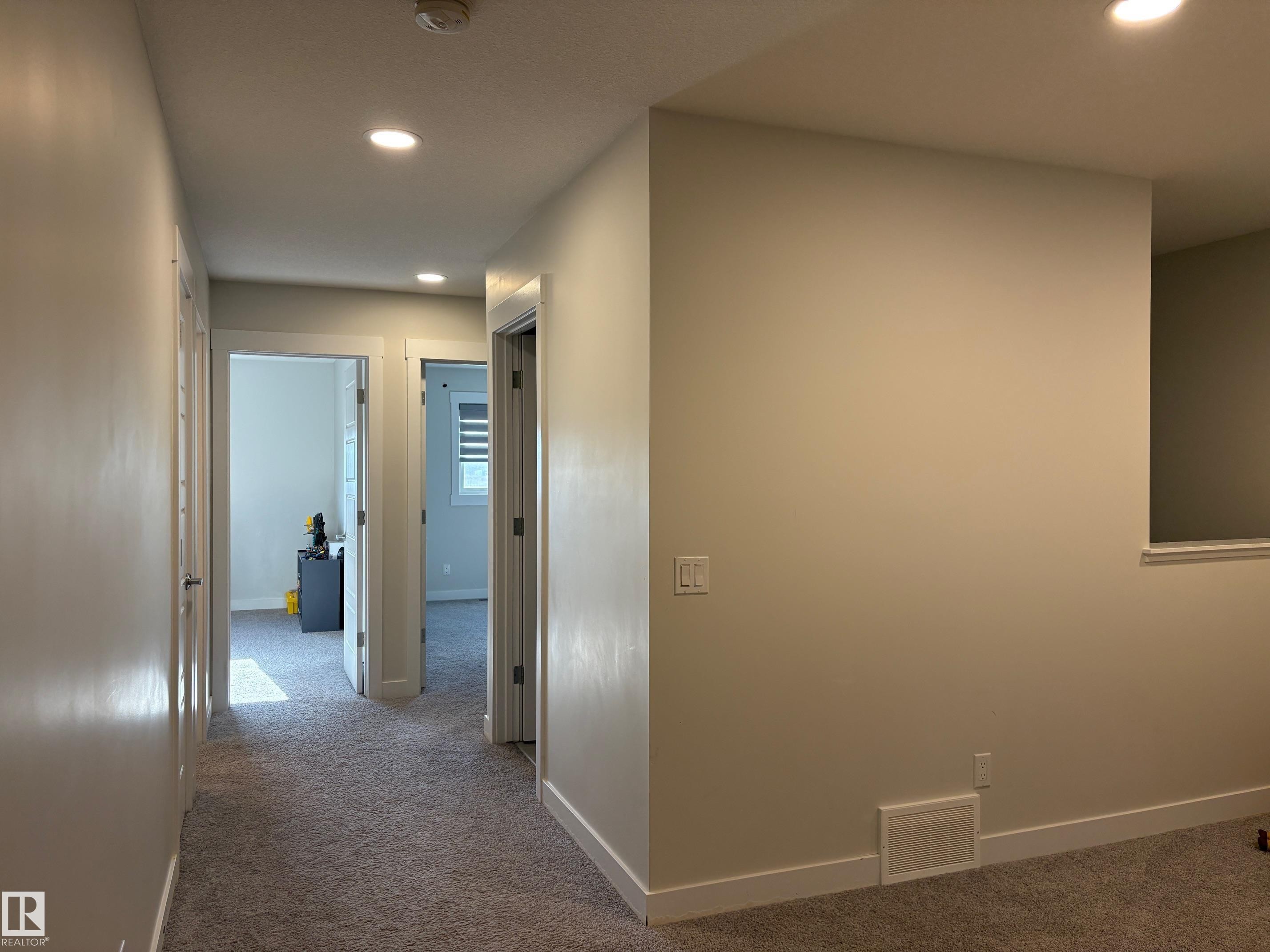 Hallway featuring recessed lighting, light gray carpet, white baseboards, and multiple doorways - 9952 227 Street, Edmonton, AB