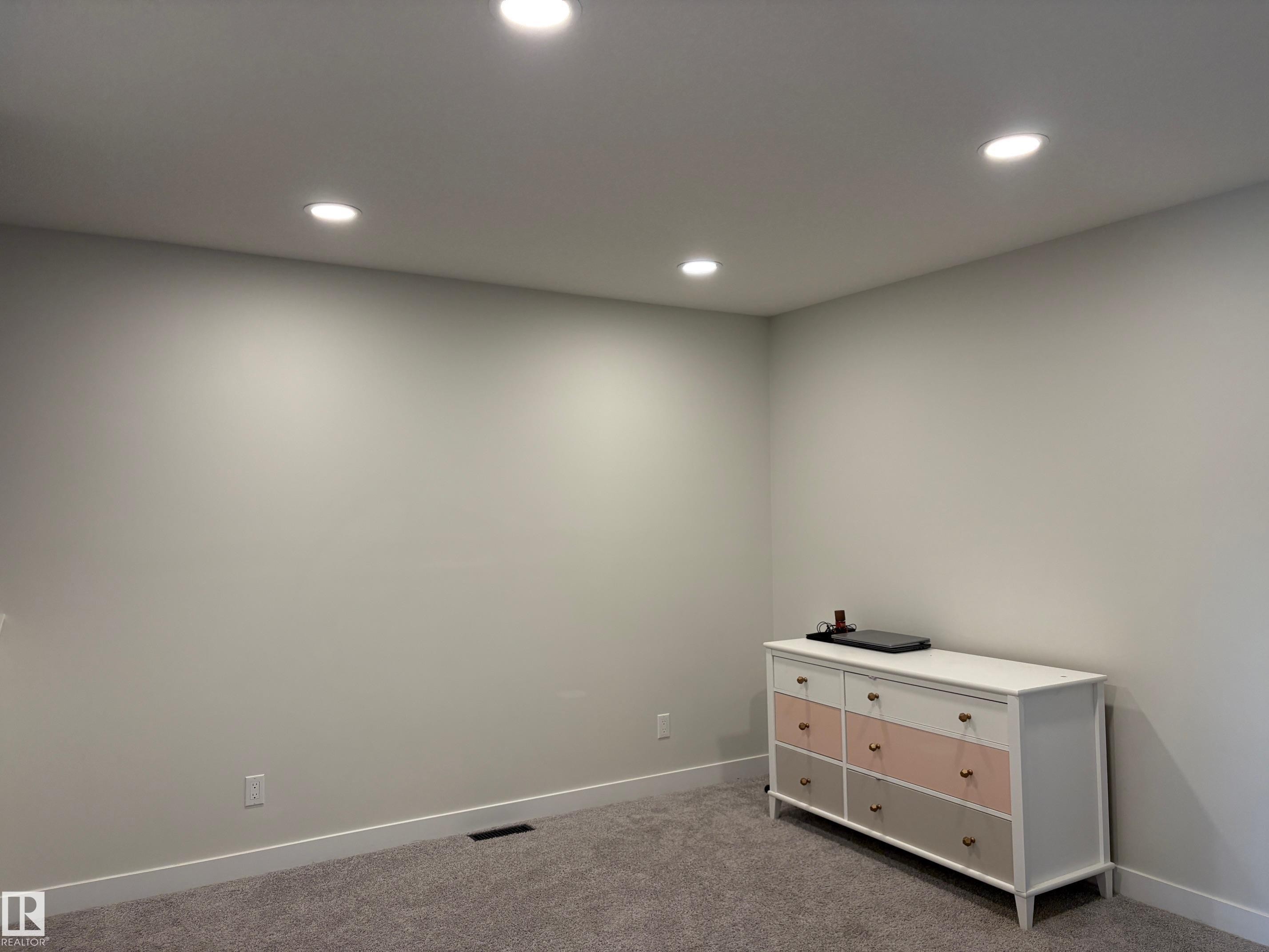 Recessed ceiling lighting illuminating a neutral-toned room with carpet flooring and white baseboards - 9952 227 Street, Edmonton, AB