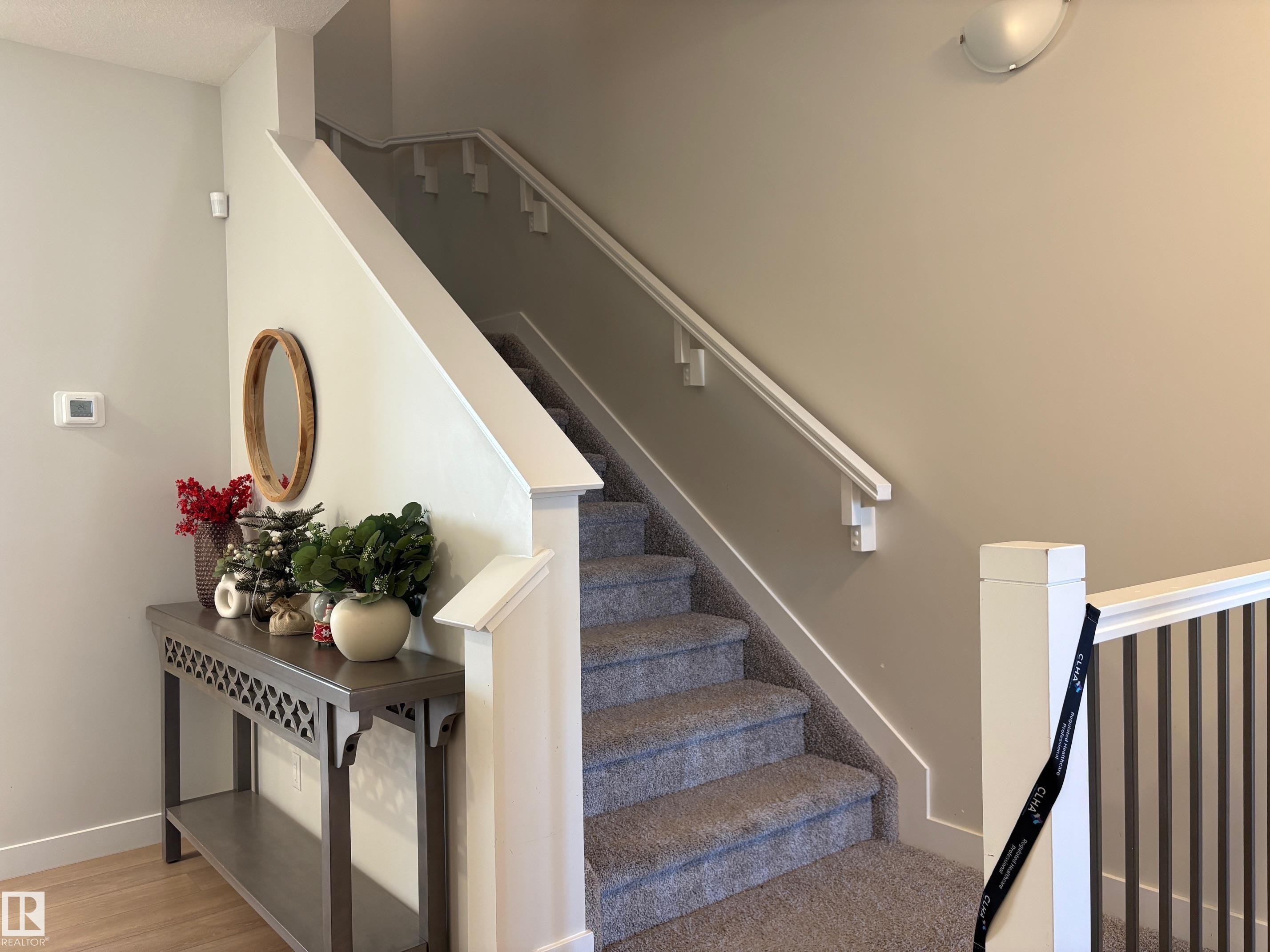 Carpeted staircase with white handrail and balusters, featuring light-toned walls and wood-finish flooring - 9952 227 Street, Edmonton, AB