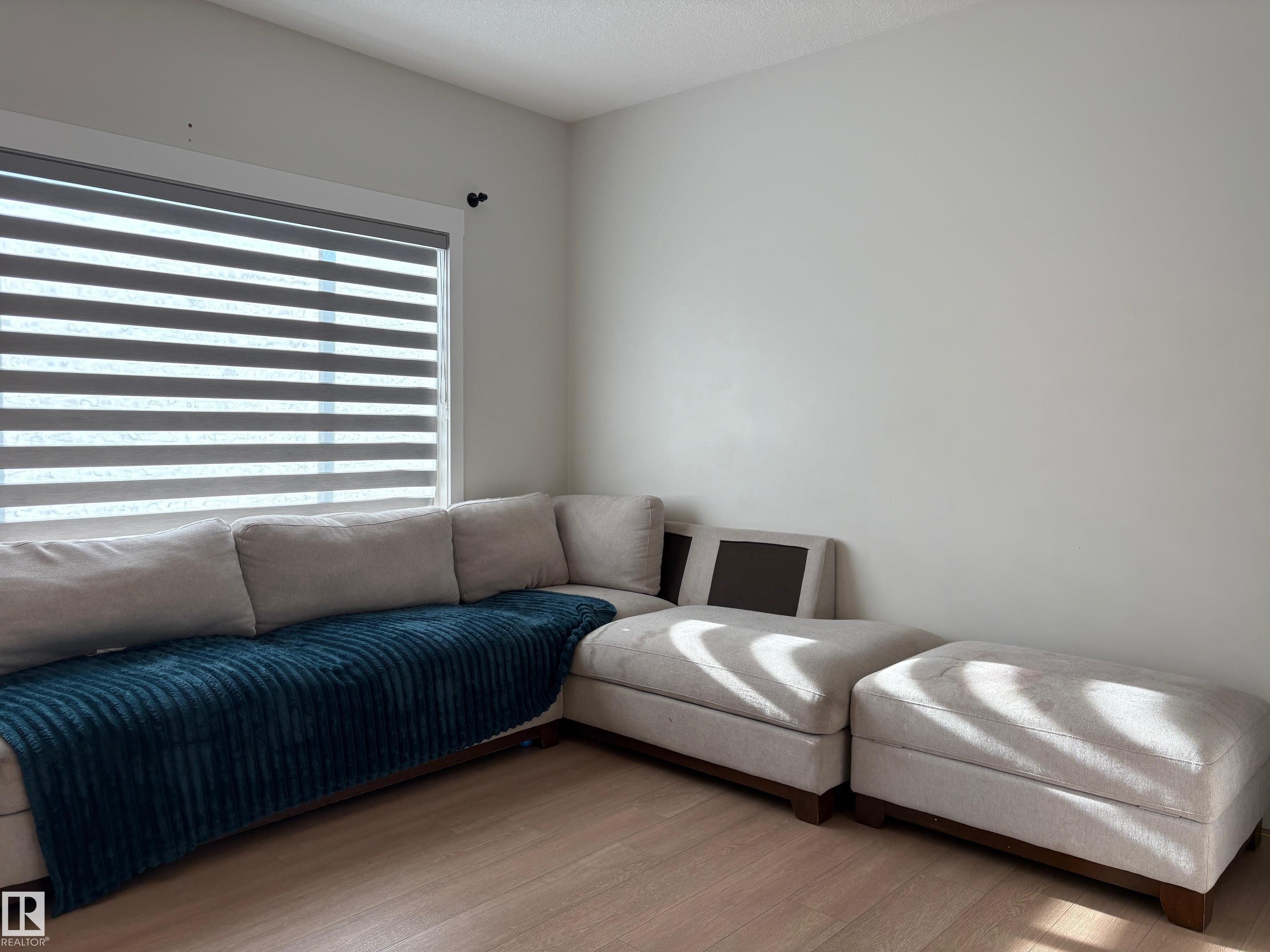 Wide window with horizontal blinds, light wood-finish flooring, and neutral wall paint - 9952 227 Street, Edmonton, AB
