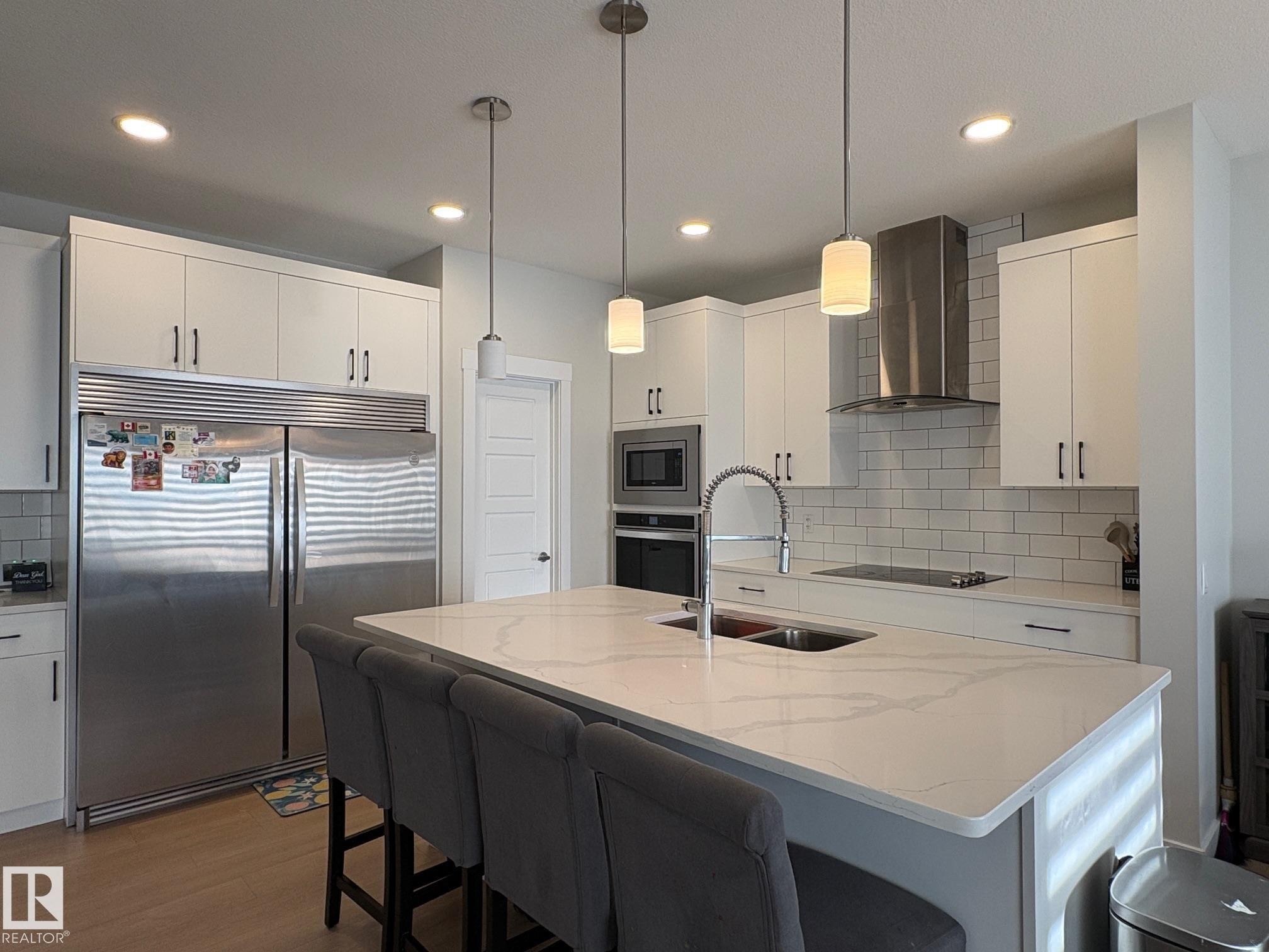 Modern kitchen featuring white cabinetry, a large center island with a double sink, stainless steel appliances, and a subway tile backsplash - 9952 227 Street, Edmonton, AB