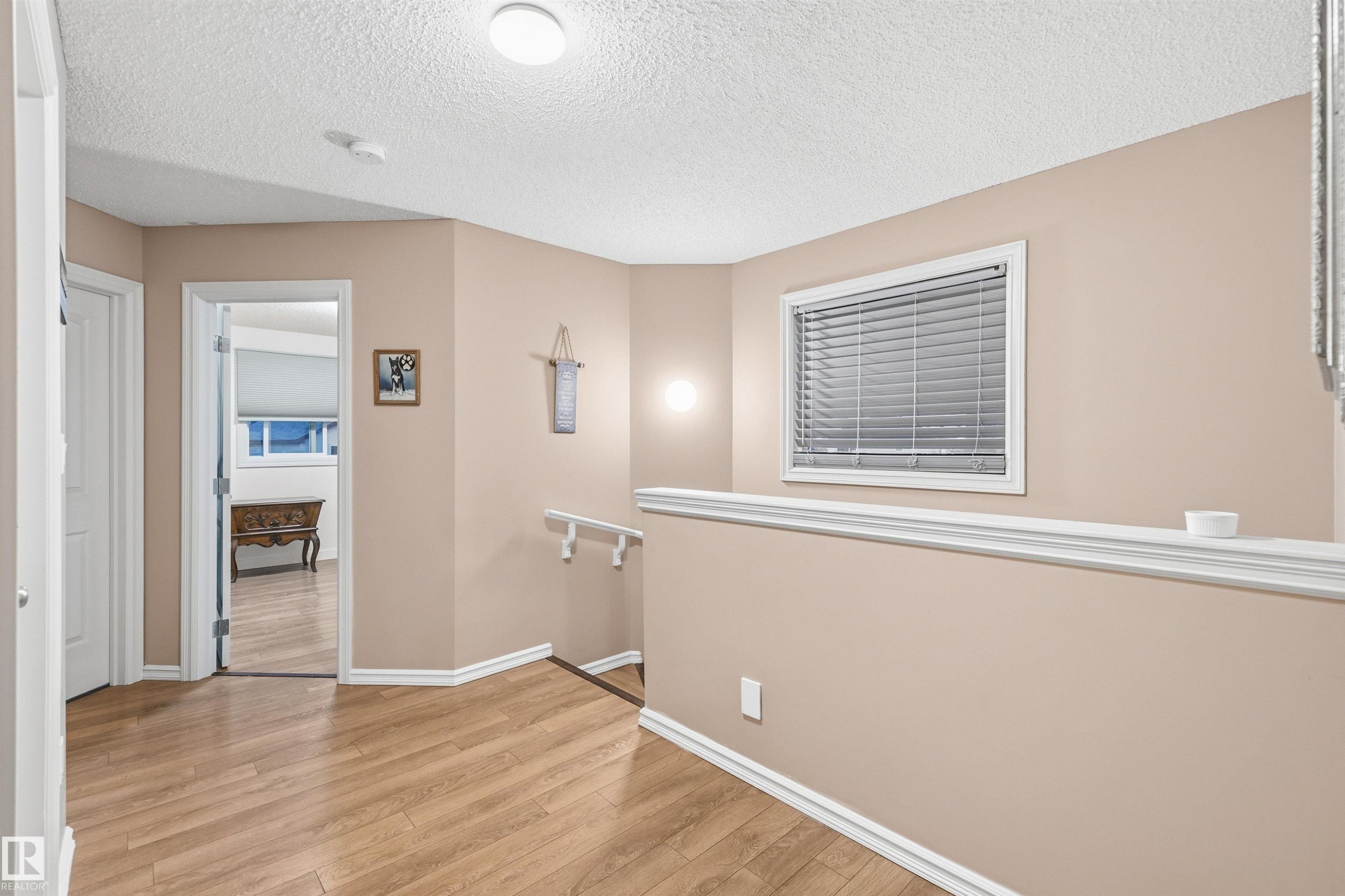 Hallway with wood-finish flooring, white baseboards, and neutral wall paint - 21207 90Ave, Edmonton, AB