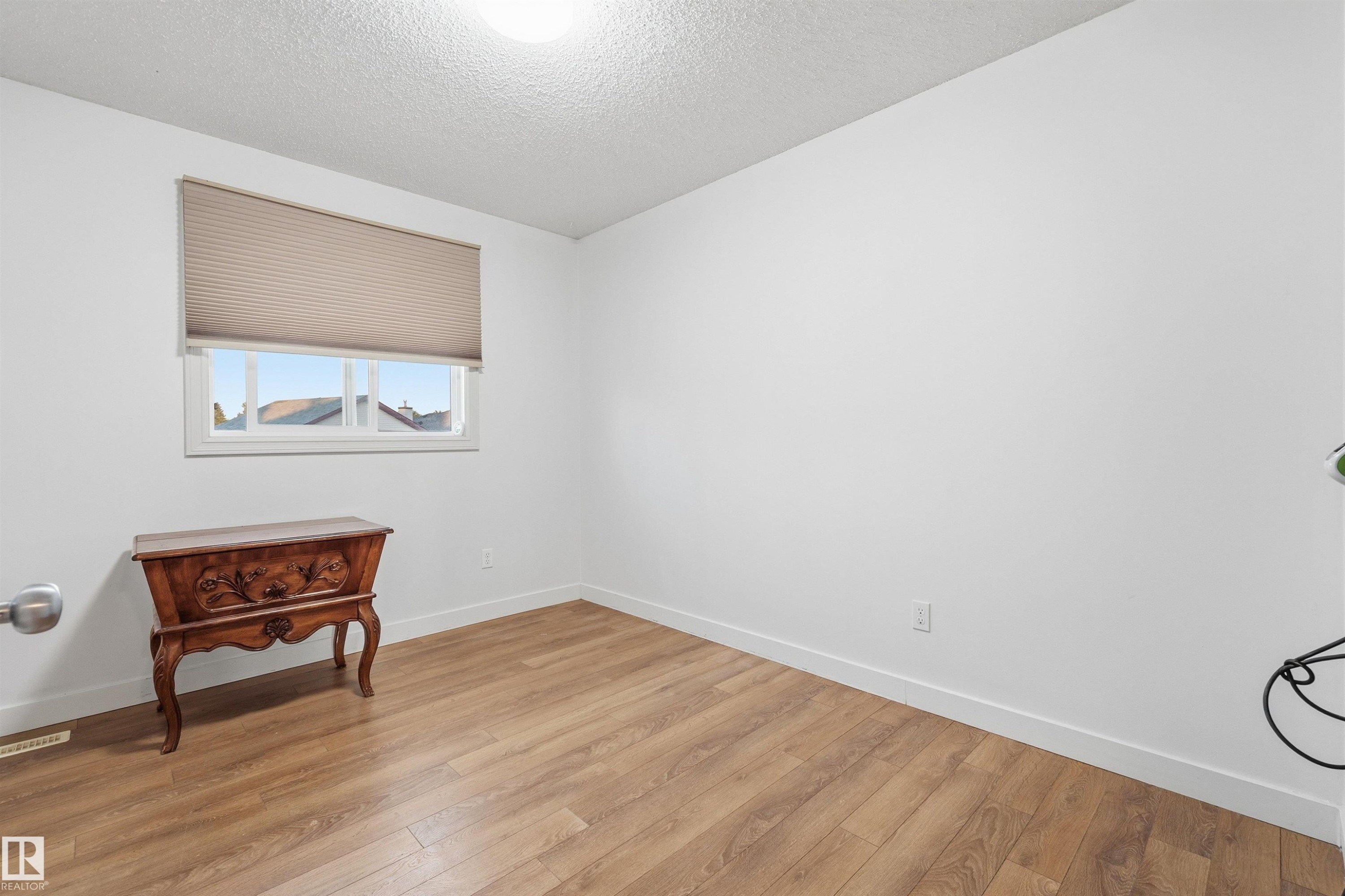 Bright room featuring wood-finish flooring and a white window frame with a pleated shade - 21207 90Ave, Edmonton, AB