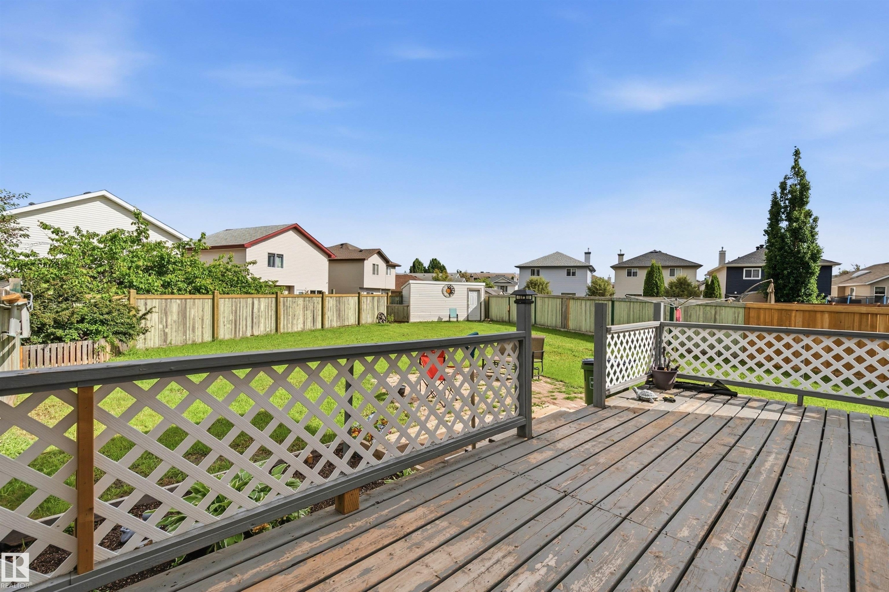 Expansive backyard featuring a wood-finish deck with lattice railing, a manicured lawn, and a storage shed - 21207 90Ave, Edmonton, AB
