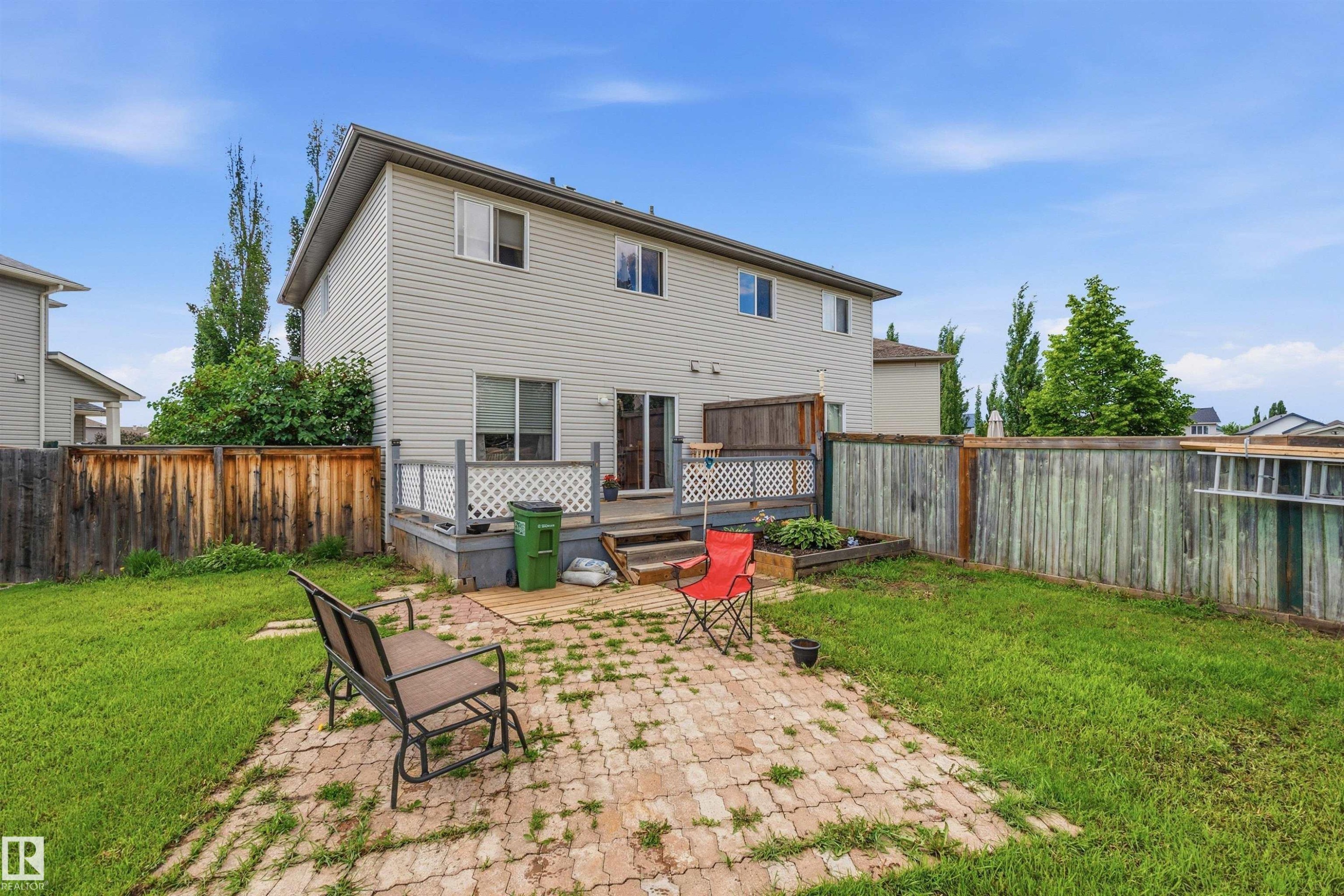 Private backyard featuring a paved patio area, green lawn, and wood privacy fencing - 21207 90Ave, Edmonton, AB