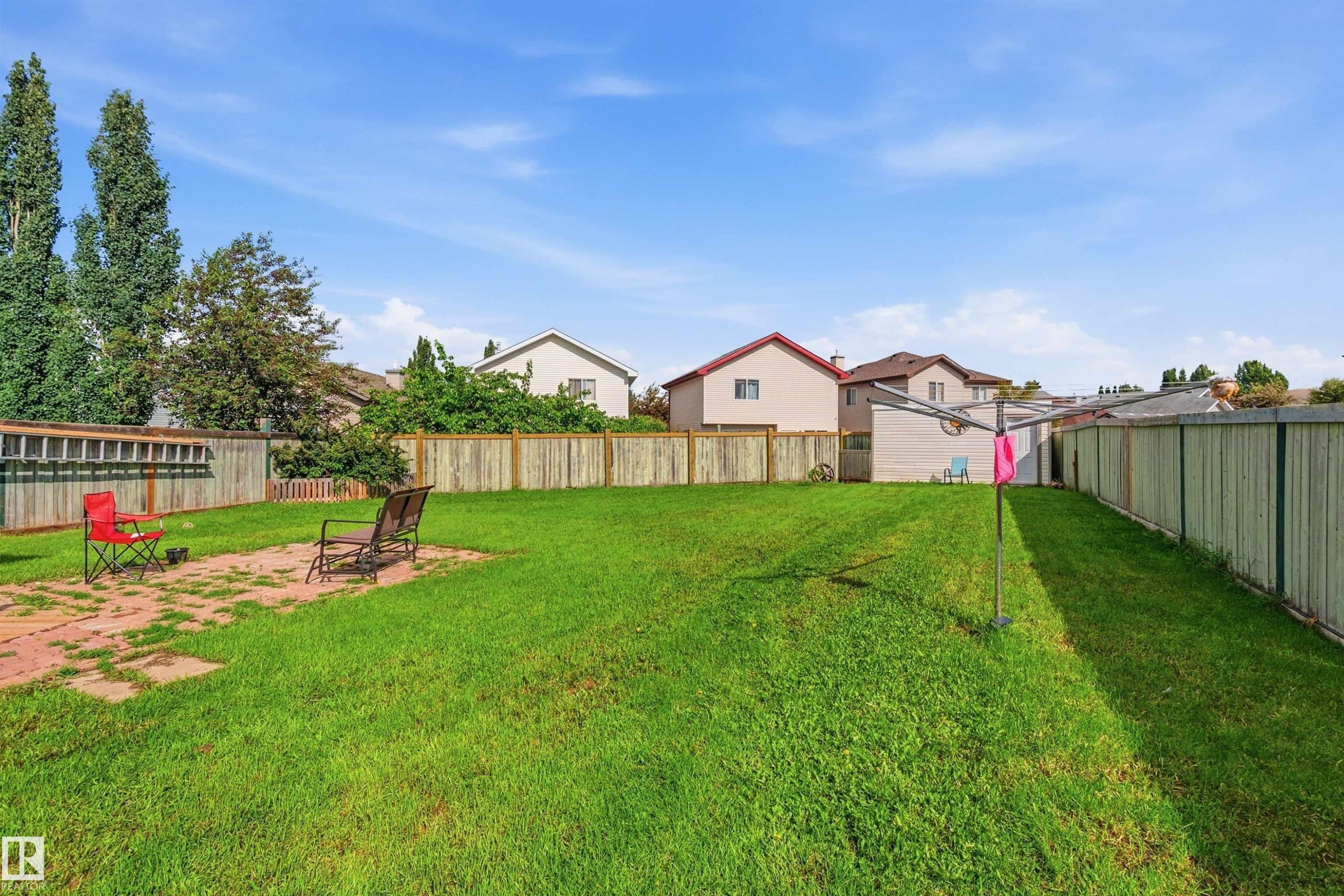 Expansive green lawn backyard featuring a patio area with pavers, perimeter wood fencing, and mature trees - 21207 90Ave, Edmonton, AB