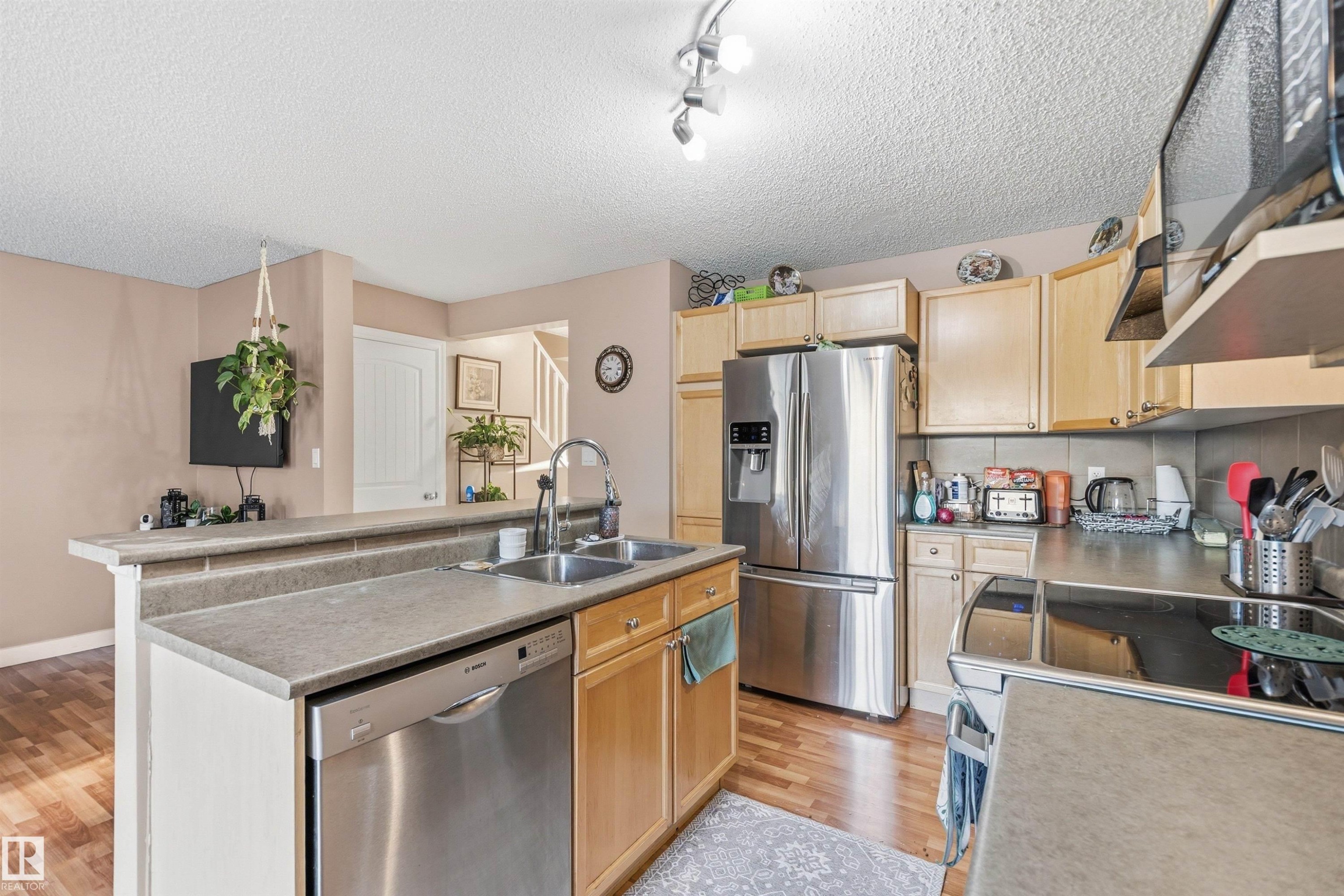 Kitchen featuring a stainless steel French door refrigerator, wood-finish flooring, and light-toned cabinetry - 21207 90Ave, Edmonton, AB