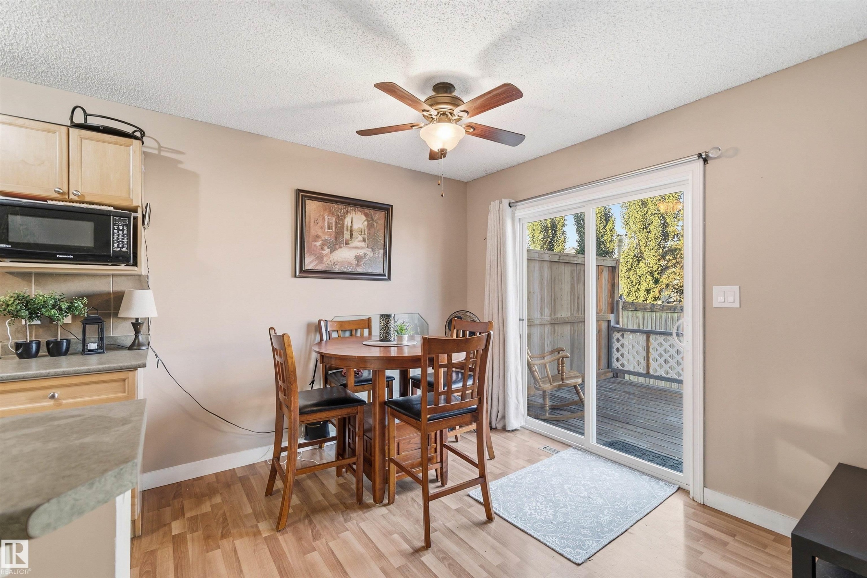 Kitchen and dining area featuring wood-finish flooring, a ceiling fan with integrated lighting, and a sliding glass door providing access to an outdoor deck - 21207 90Ave, Edmonton, AB