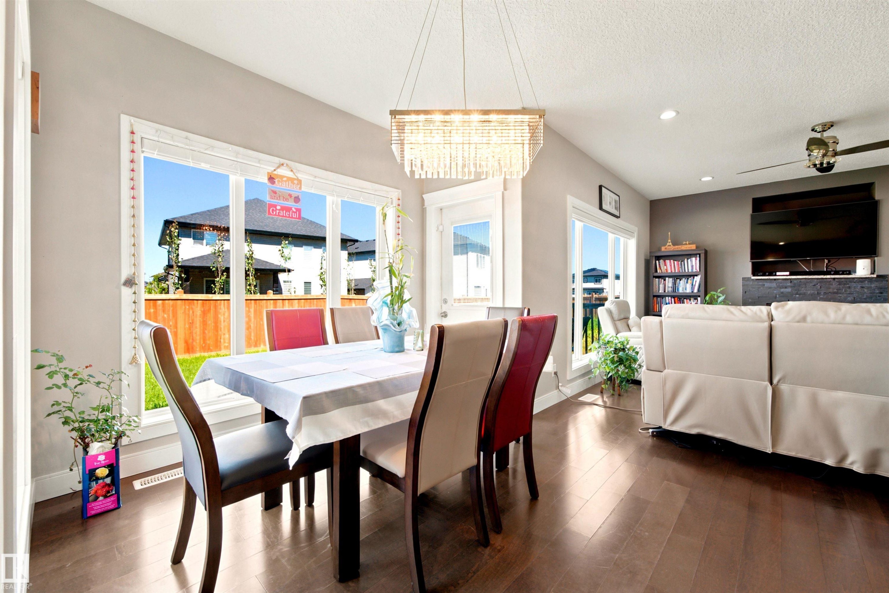 Open-concept dining area featuring wood-finish flooring and a rectangular crystal chandelier - 5110 Rue Eaglemont, Beaumont, AB