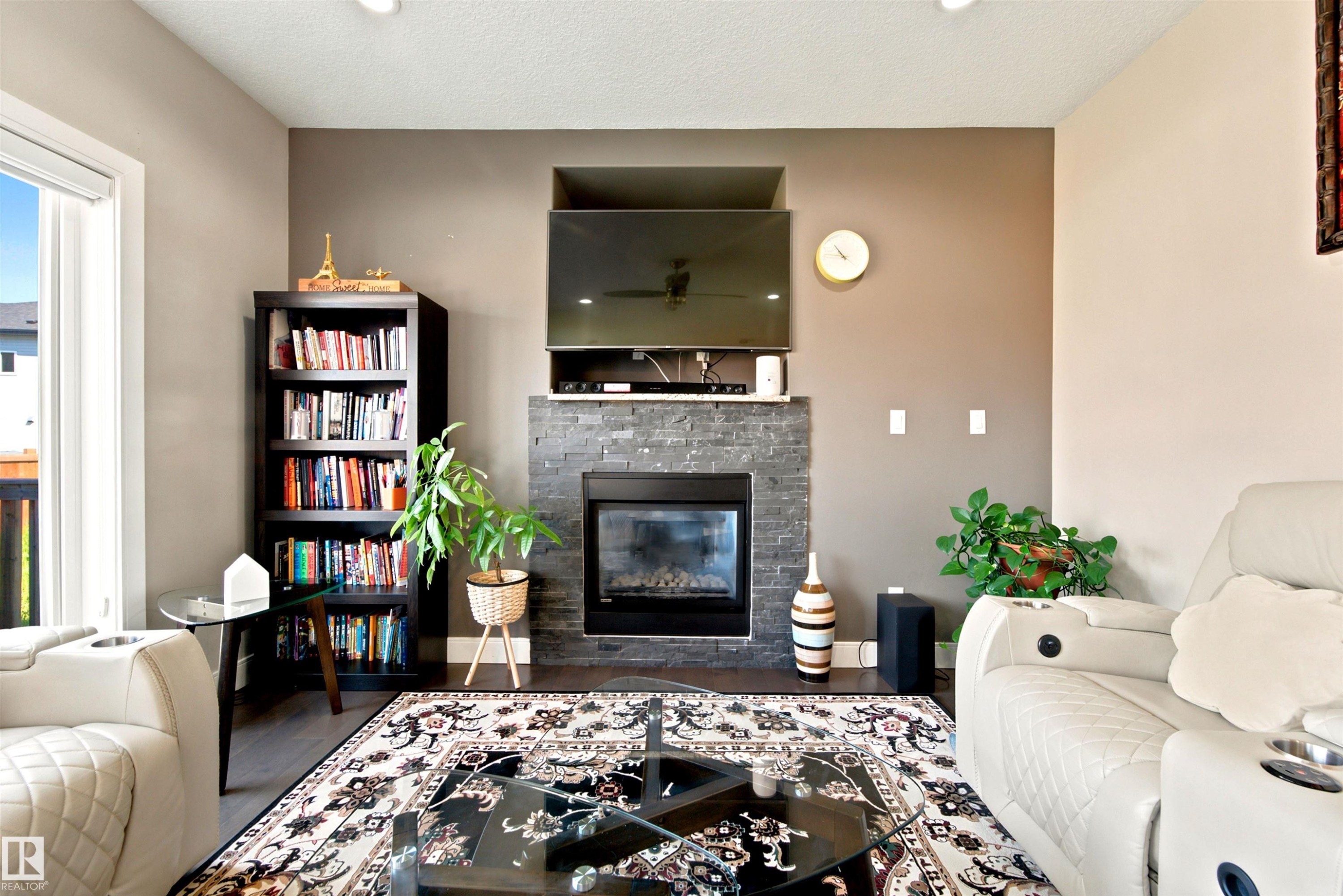 Living area featuring a floor-to-ceiling slate-look tile fireplace surround with a built-in electric fireplace, recessed ceiling lighting, and wood-finish flooring - 5110 Rue Eaglemont, Beaumont, AB