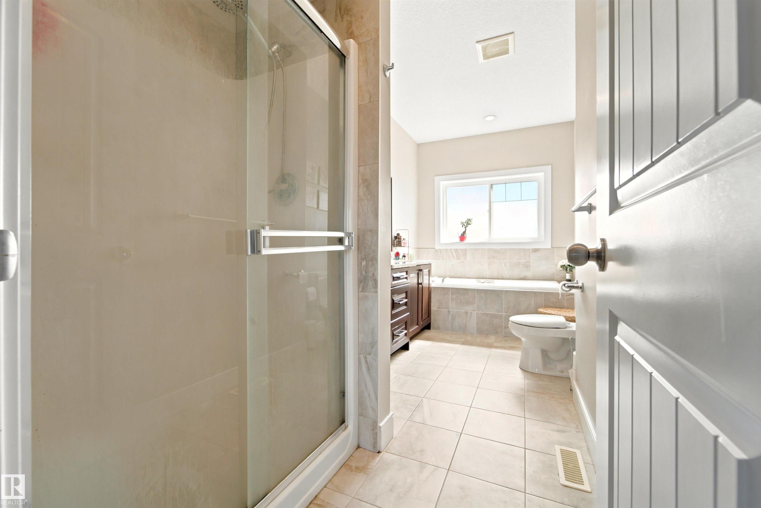 Bathroom featuring a glass-enclosed shower, a built-in soaking tub, a window above the tub, a vanity with a dark wood-finish cabinet, and light-toned tile flooring - 5110 Rue Eaglemont, Beaumont, AB