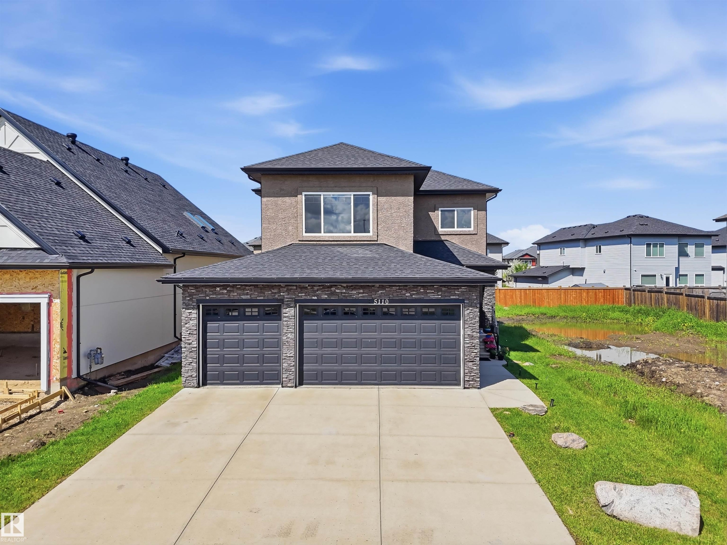 Contemporary stucco and stone-clad residence featuring a spacious two-car garage with panel doors - 5110 Rue Eaglemont, Beaumont, AB