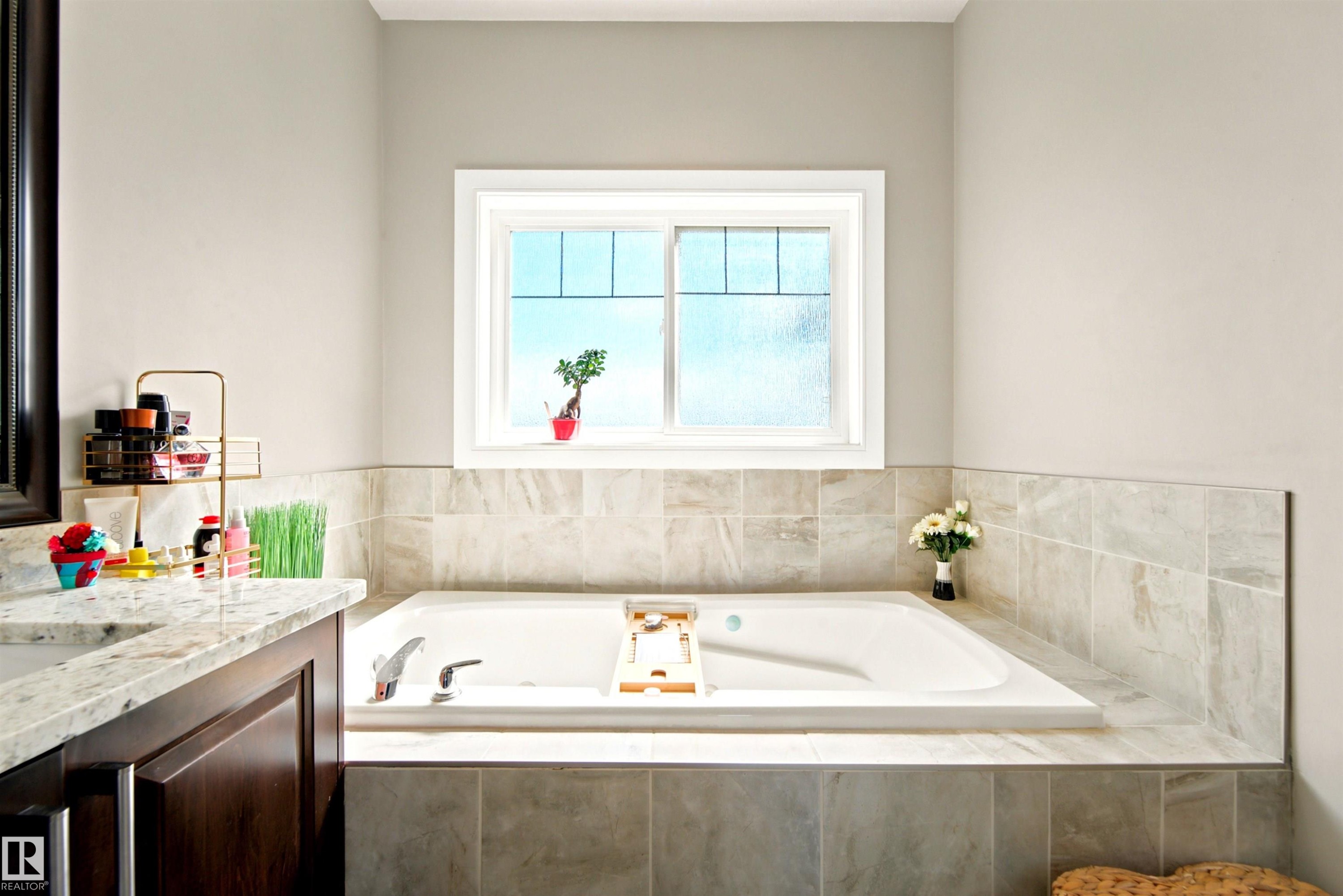Soaking tub with a tiled surround, framed by a white window - 5110 Rue Eaglemont, Beaumont, AB