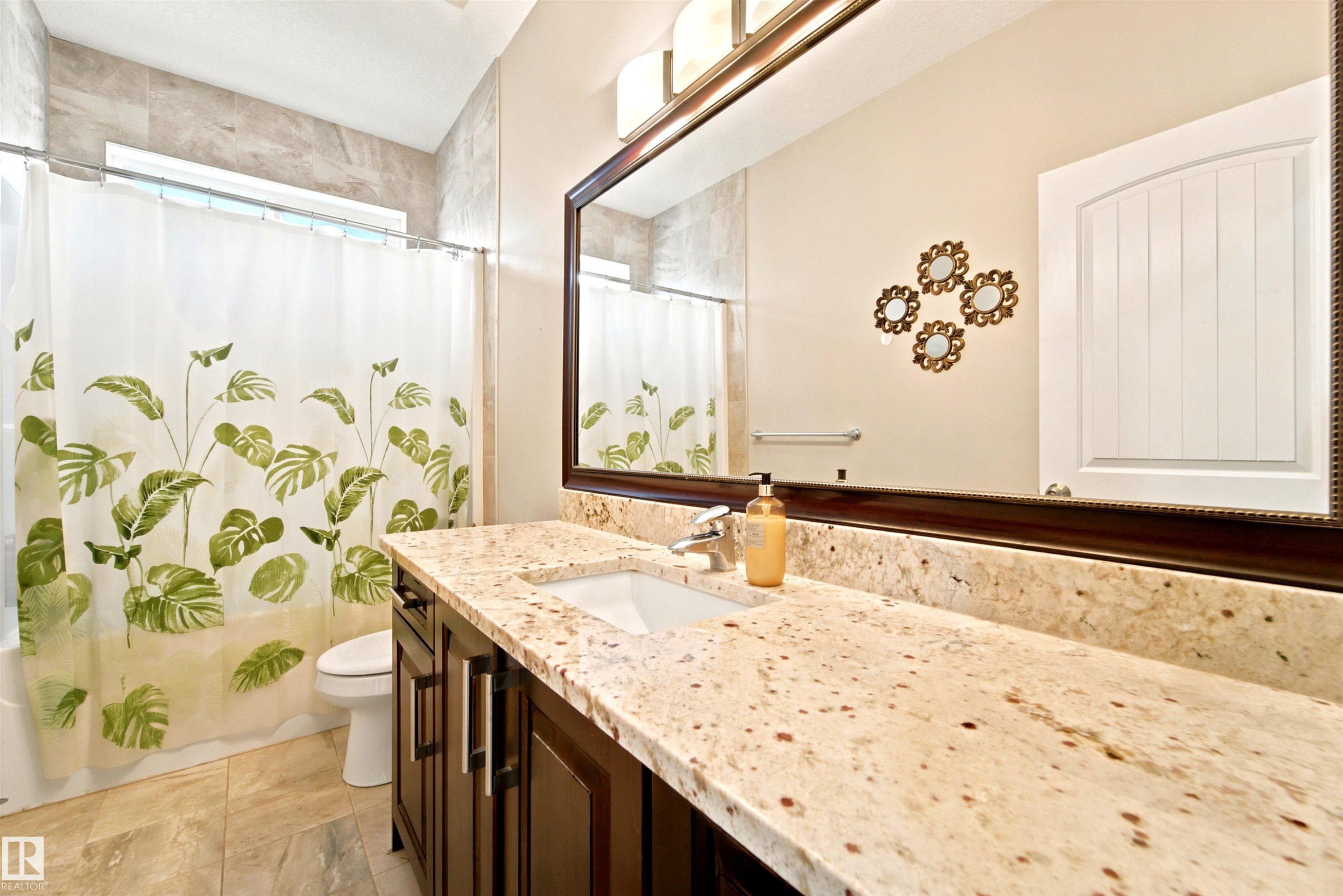 Spacious bathroom featuring a dark wood-finish vanity with a light-toned countertop, a large framed mirror, and a tiled shower surround with an integrated window - 5110 Rue Eaglemont, Beaumont, AB