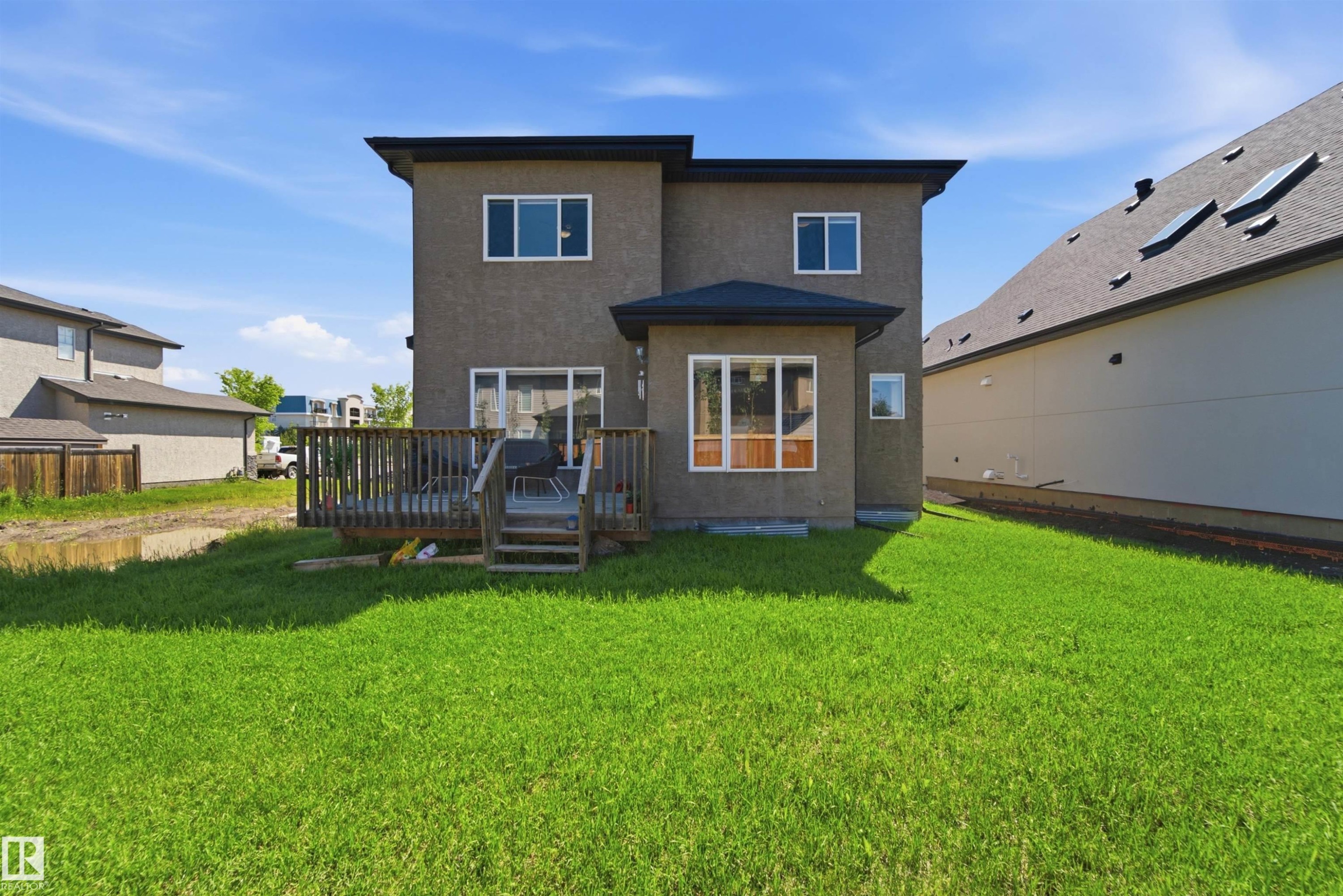 Back exterior featuring a large green lawn, multi-level wood deck, and a sunroom extension - 5110 Rue Eaglemont, Beaumont, AB