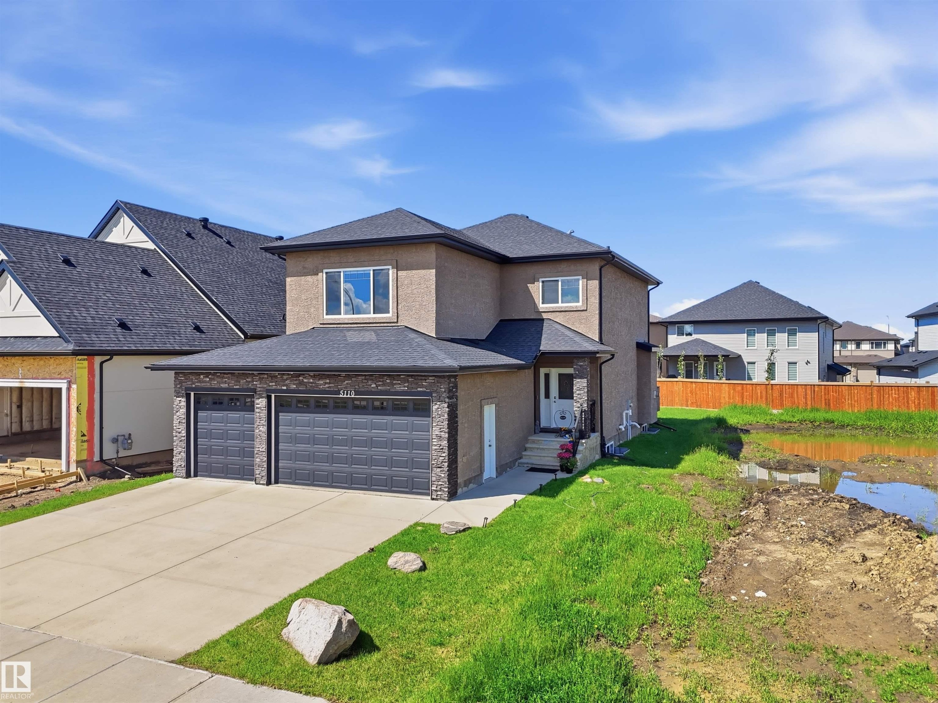Contemporary residence featuring a stucco exterior with stone accents, a two-car garage, and a concrete driveway - 5110 Rue Eaglemont, Beaumont, AB