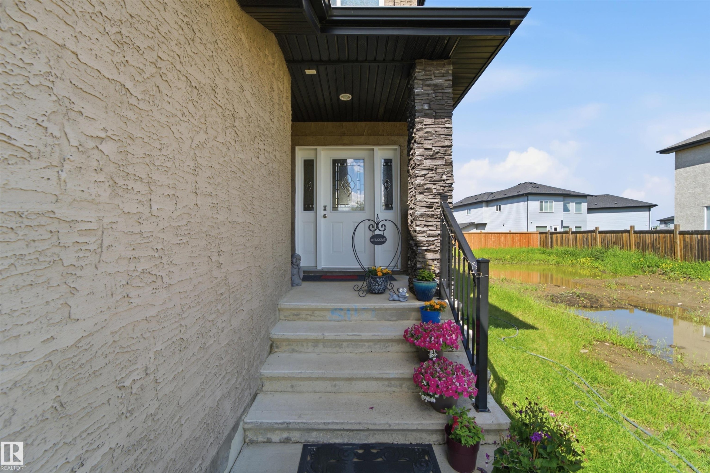Front entry featuring a white door with decorative glass, concrete steps, a black metal railing, and a stone-clad pillar - 5110 Rue Eaglemont, Beaumont, AB