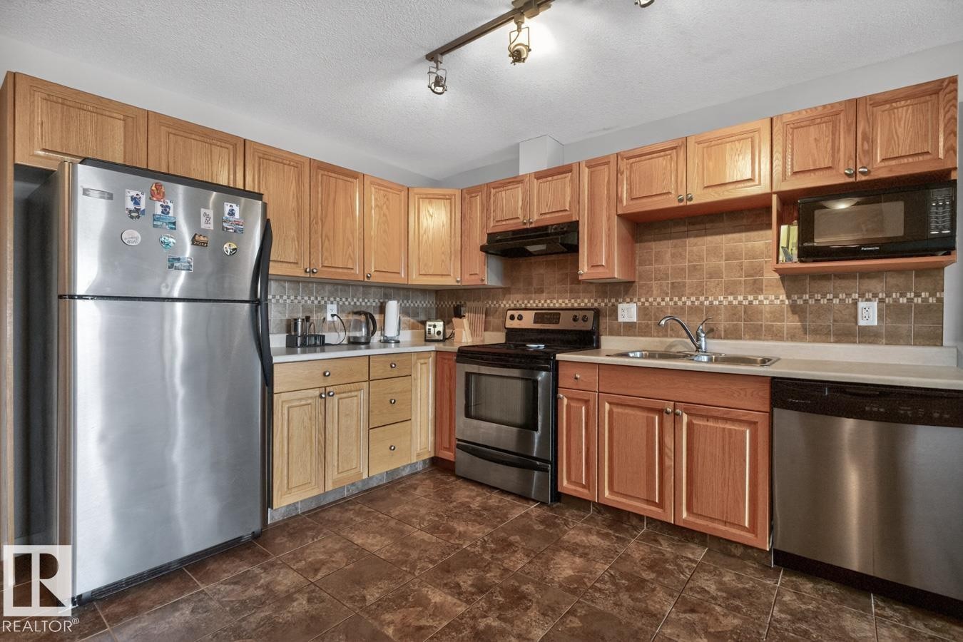 Kitchen featuring wood-finish cabinetry, stainless steel appliances, a tiled backsplash, and recessed lighting - 320 5005 165 Avenue, Edmonton, AB - Indoor Photo Showing Kitchen