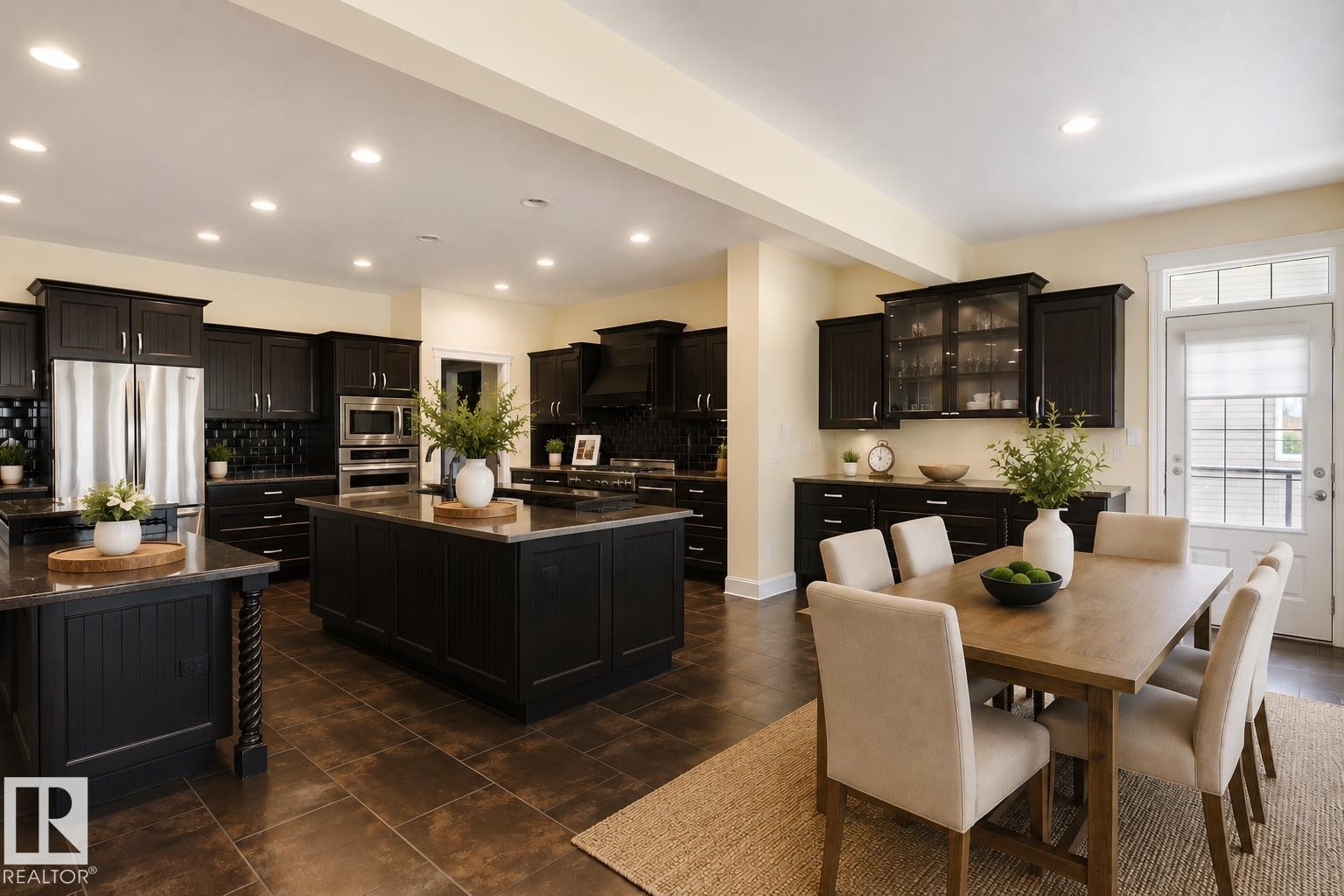 Open-concept kitchen and dining area featuring dark cabinetry, stainless steel appliances, two kitchen islands with solid surface countertops, recessed lighting, and a glass-paneled door - 3438 West Landing Landing, Edmonton, AB