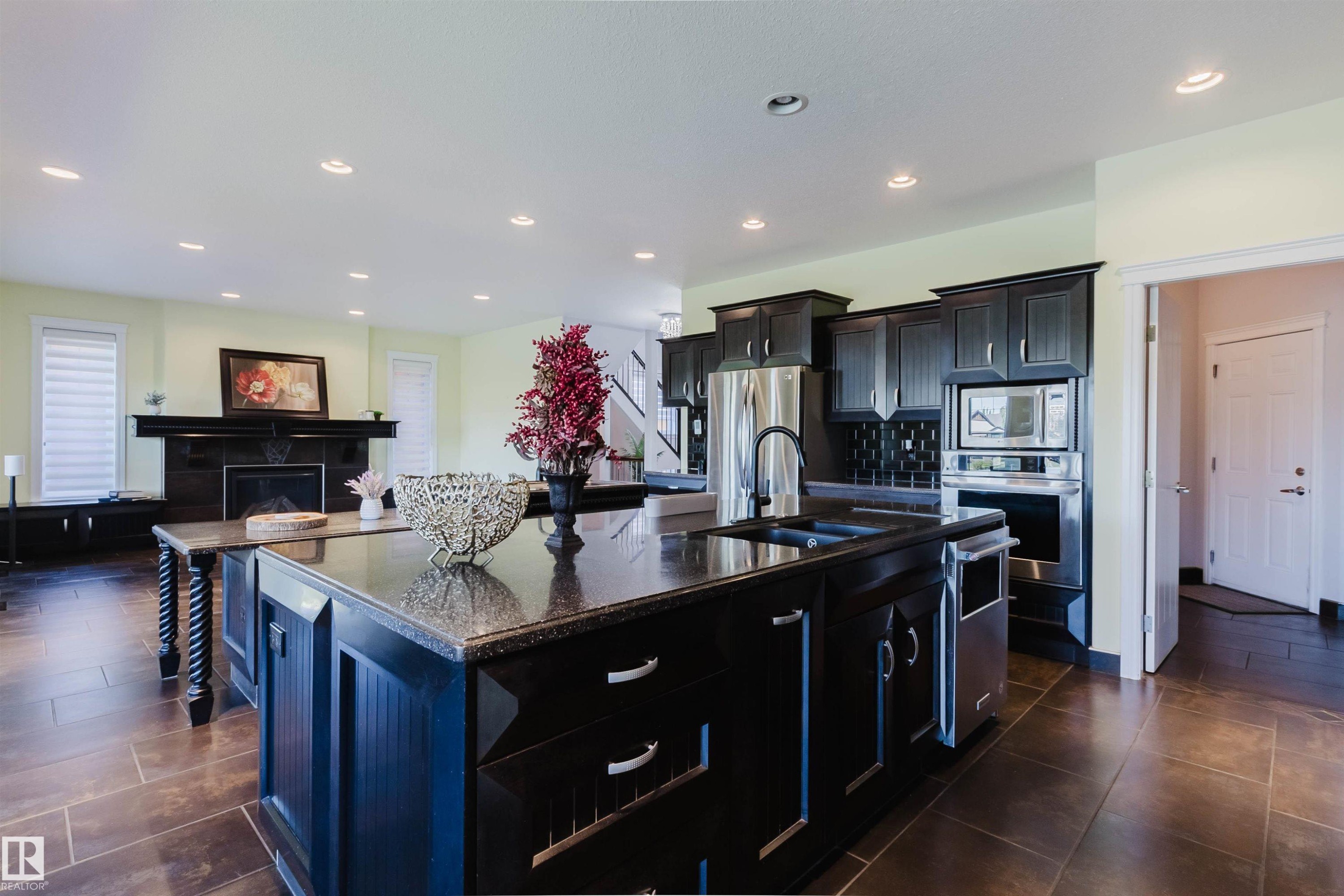 Kitchen featuring dark cabinetry, stainless steel appliances, granite countertops, and a large central island with an integrated sink - 3438 West Landing Landing, Edmonton, AB