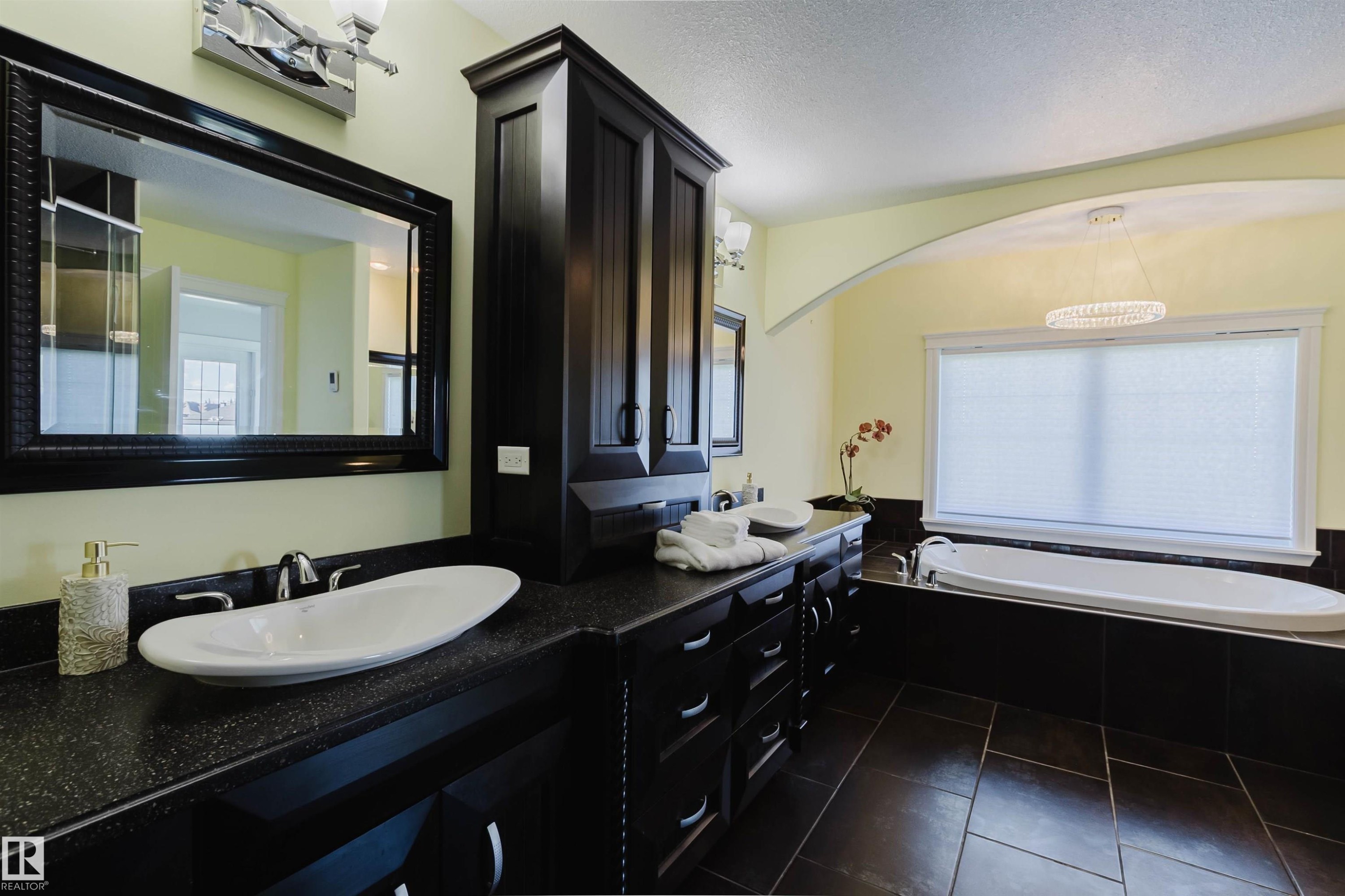 Bathroom featuring a dual vanity with vessel sinks, dark wood-finish cabinetry, and a spacious built-in tub - 3438 West Landing Landing, Edmonton, AB