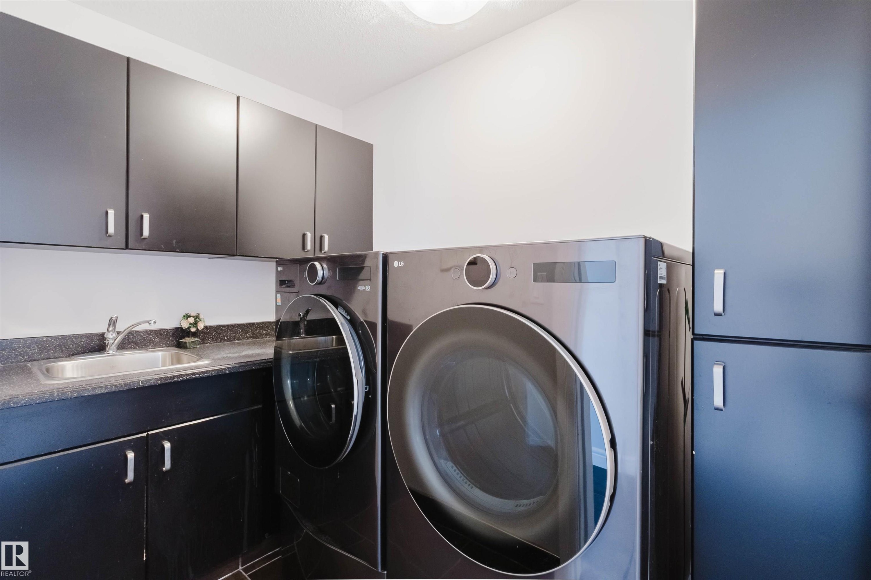 Laundry area featuring dark cabinetry, a countertop with an integrated sink, and modern appliances - 3438 West Landing Landing, Edmonton, AB
