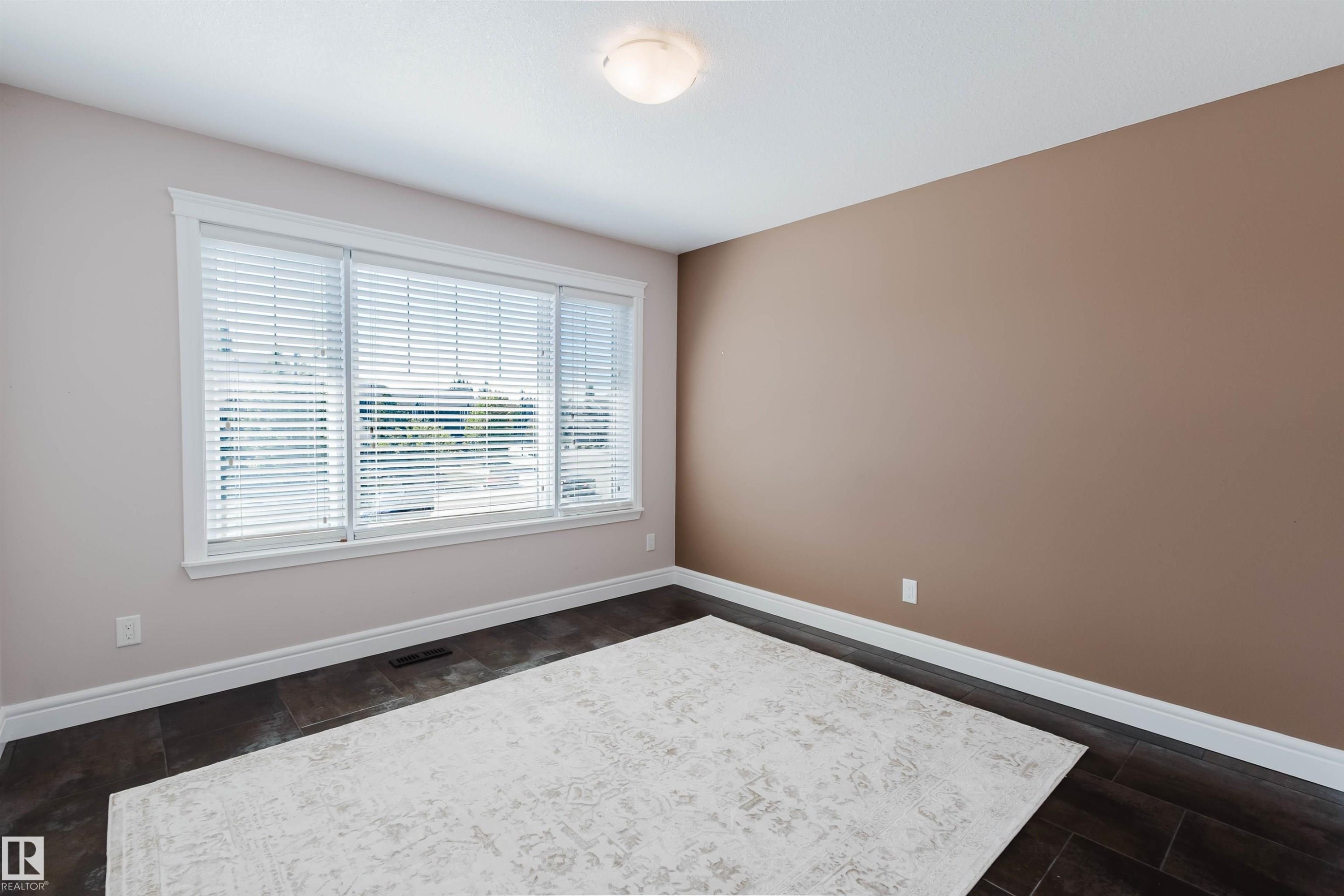 Spacious room featuring dark wood-look flooring, a large window with white blinds, and a neutral color palette - 3438 West Landing Landing, Edmonton, AB