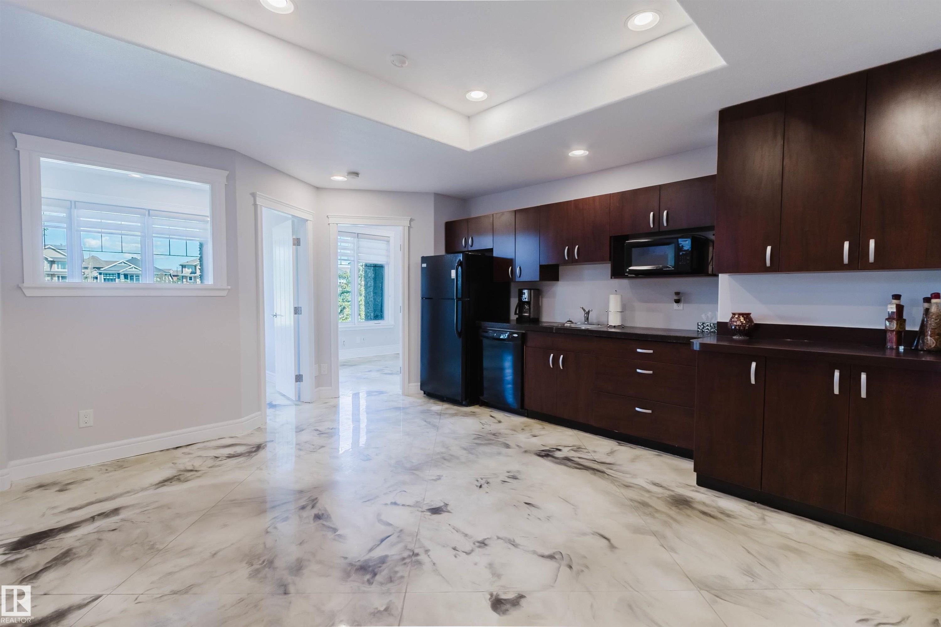 Spacious room featuring elegant veined flooring, a full-height dark wood cabinetry wall with integrated appliances, recessed lighting, and a window with white blinds - 3438 West Landing Landing, Edmonton, AB