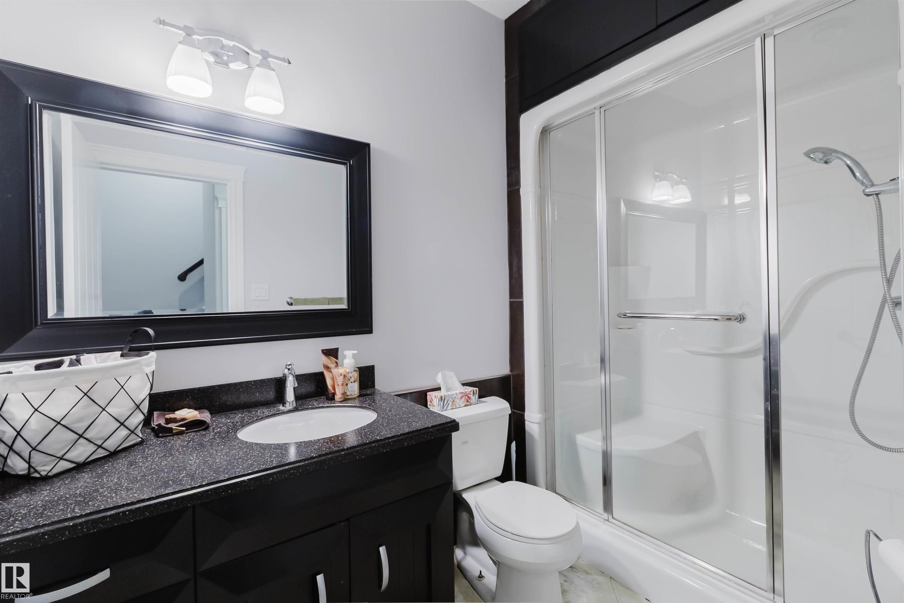 Bathroom featuring a dark vanity with a light-speckled countertop, an undermount sink, and a framed wall mirror - 3438 West Landing Landing, Edmonton, AB
